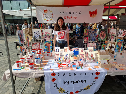 Artist’s colourful market stall at Swan Market Utrecht with handmade animal mugs, cards, prints and accessories on display.