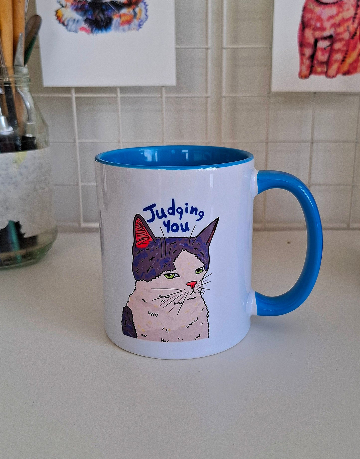 Mug with a cat illustration and text 'Judging You' on a kitchen counter.