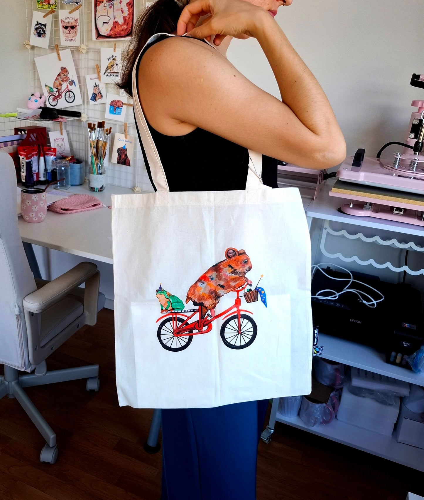 Person holding a tote bag with a hamster riding a bike design.