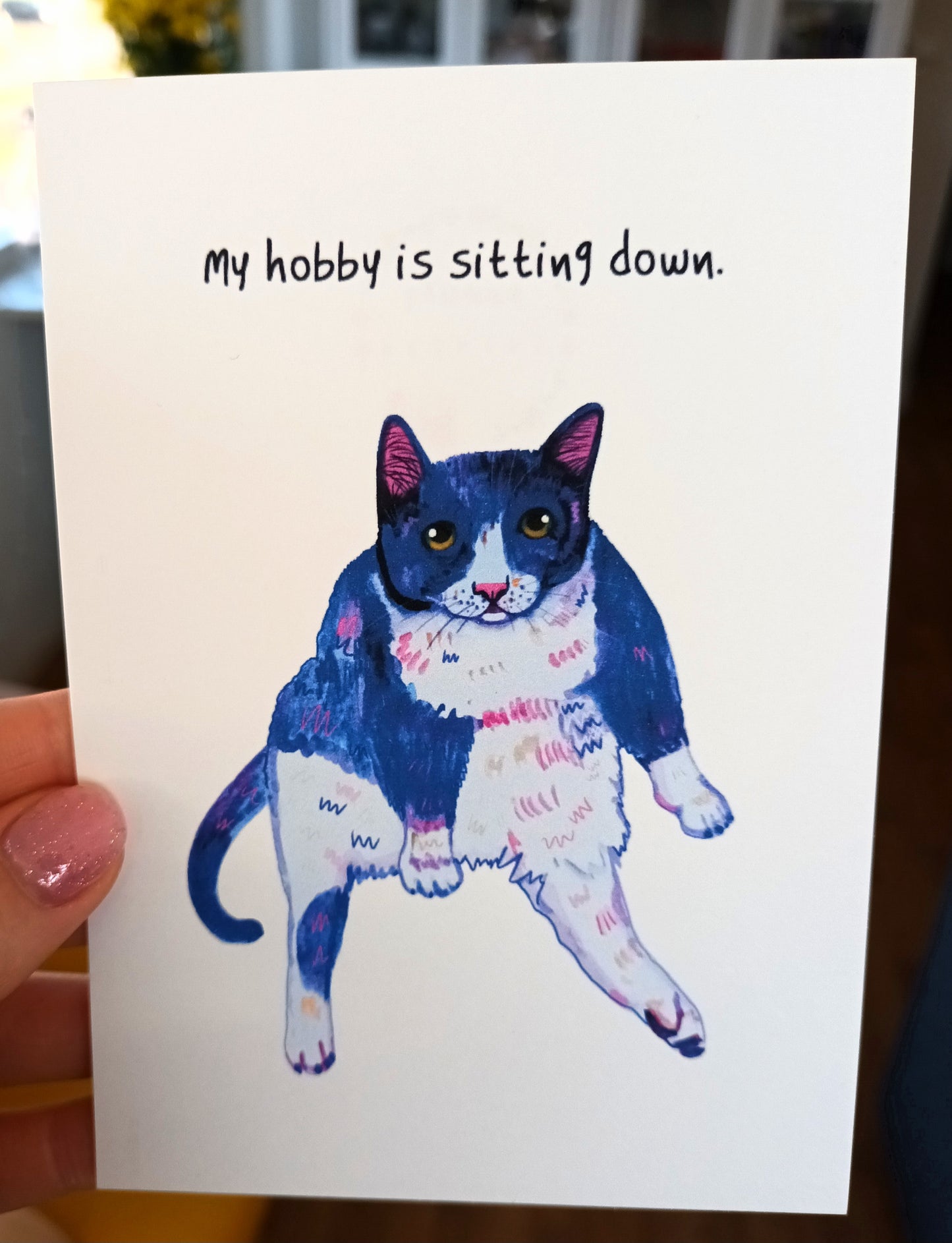 Funny greeting card featuring a sassy tuxedo cat with ‘My Hobby is Sitting Down’ text, printed on eco-friendly paper held by hand