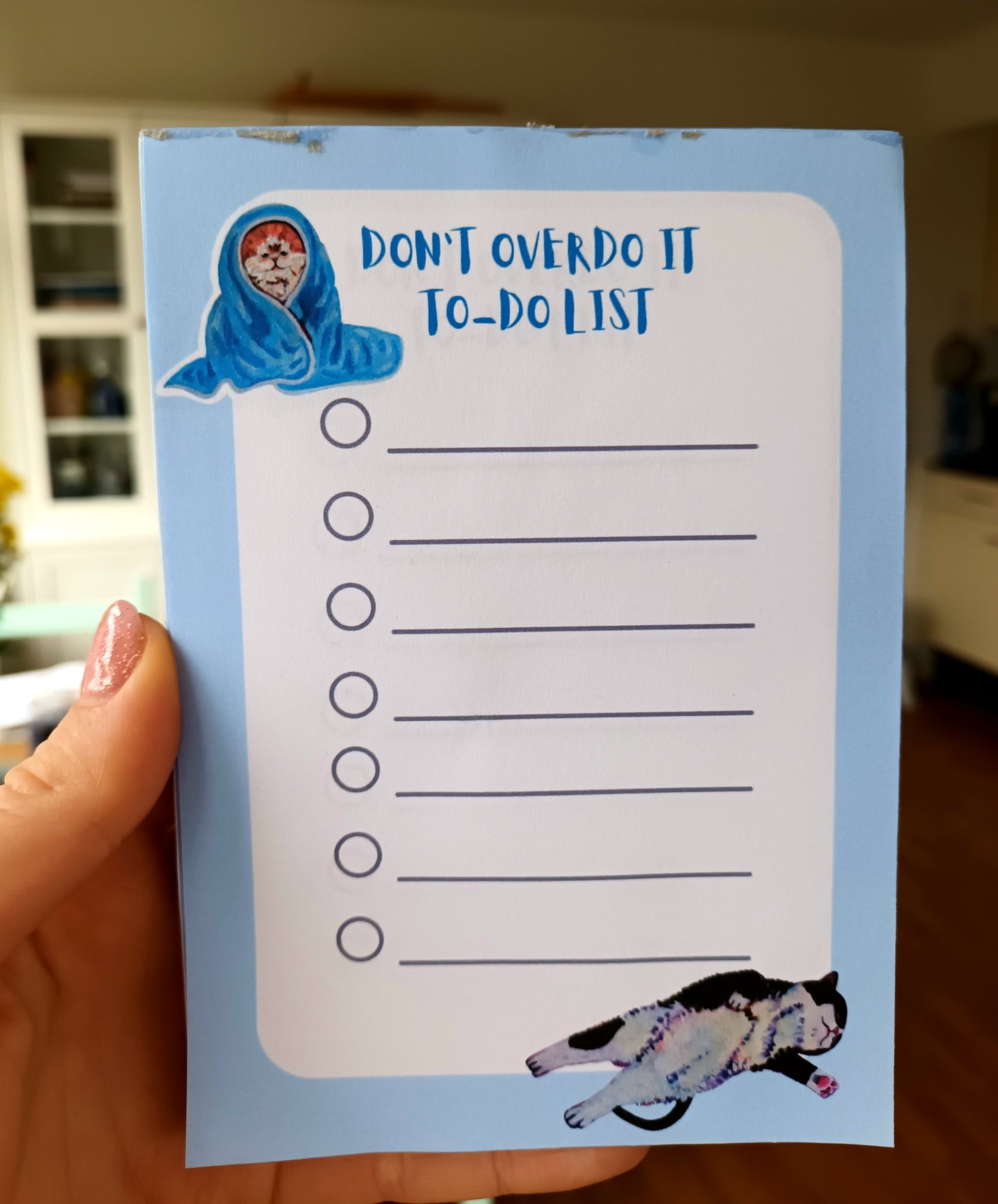 Funny cat-themed to-do list notepad with dramatic cats, light-blue background, available in 30 or 50 pages, printed on eco-friendly paper with a sturdy cardboard back held by hand