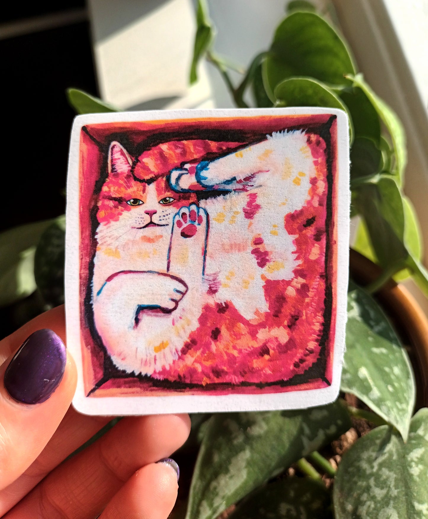 Cute orange cat in a box sticker, hand-drawn design on waterproof vinyl, perfect for decorating laptops and notebooks, held by hand.