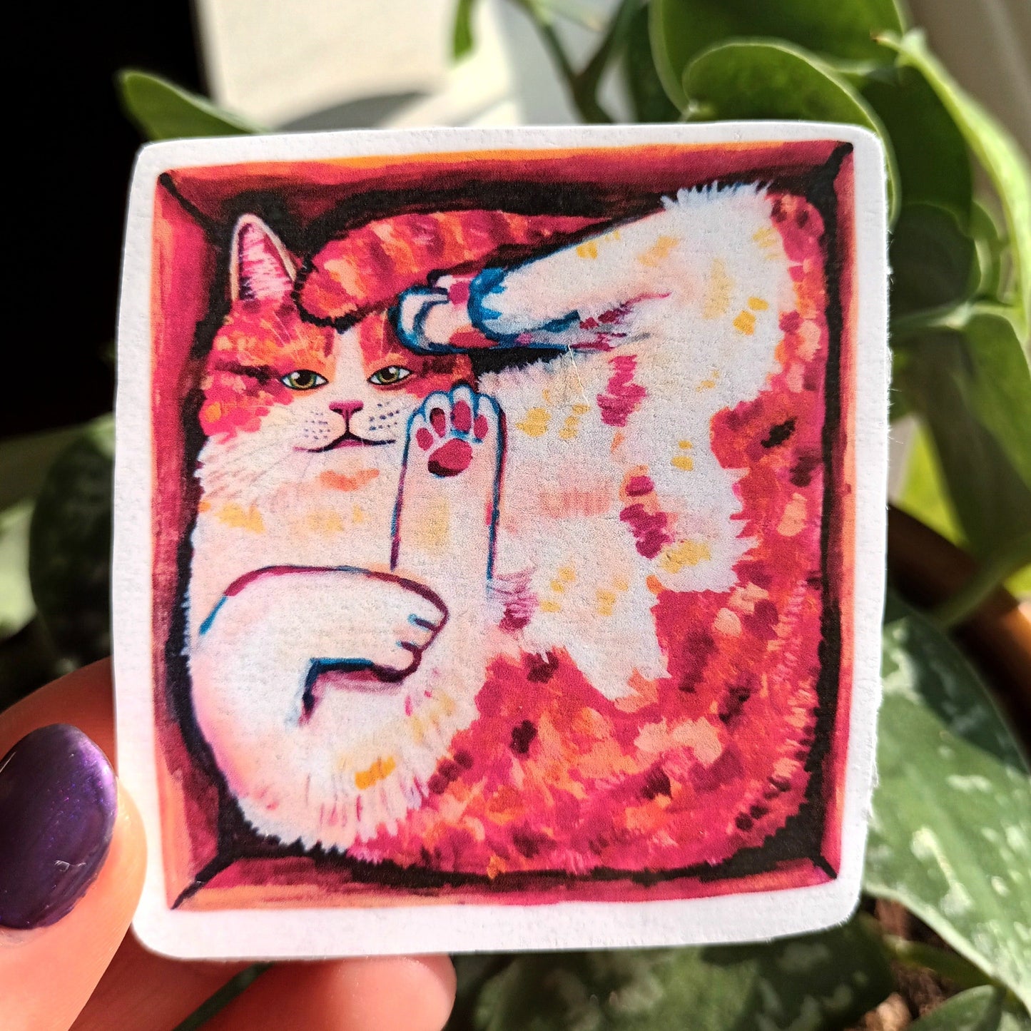Cute orange cat in a box sticker, hand-drawn design on waterproof vinyl, perfect for decorating laptops and notebooks, held by hand.