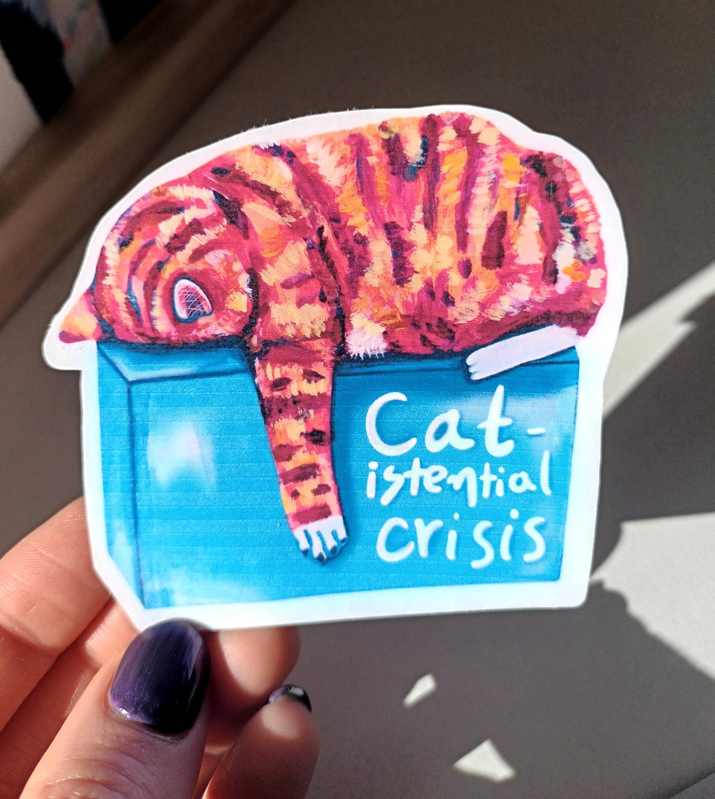 Cute orange cat sticker with a humorous existential crisis theme, hand-drawn on waterproof vinyl, held by hand.