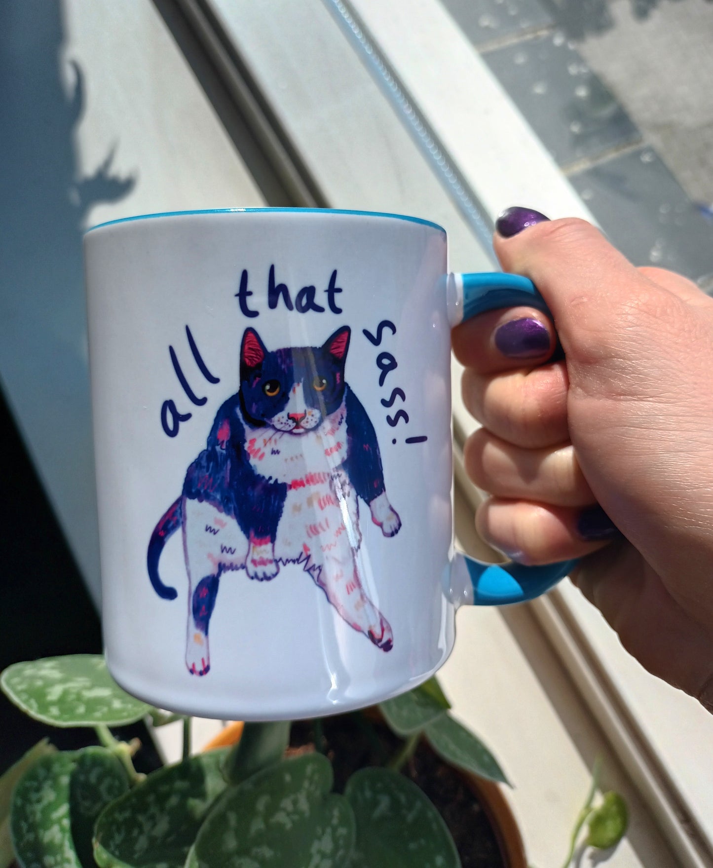 "All That Sass" mug featuring a sassy sitting cat. Handmade ceramic mug with a bold blue handle and interior. Perfect for cat lovers and coffee enthusiasts. Dishwasher and microwave safe, held by hand.