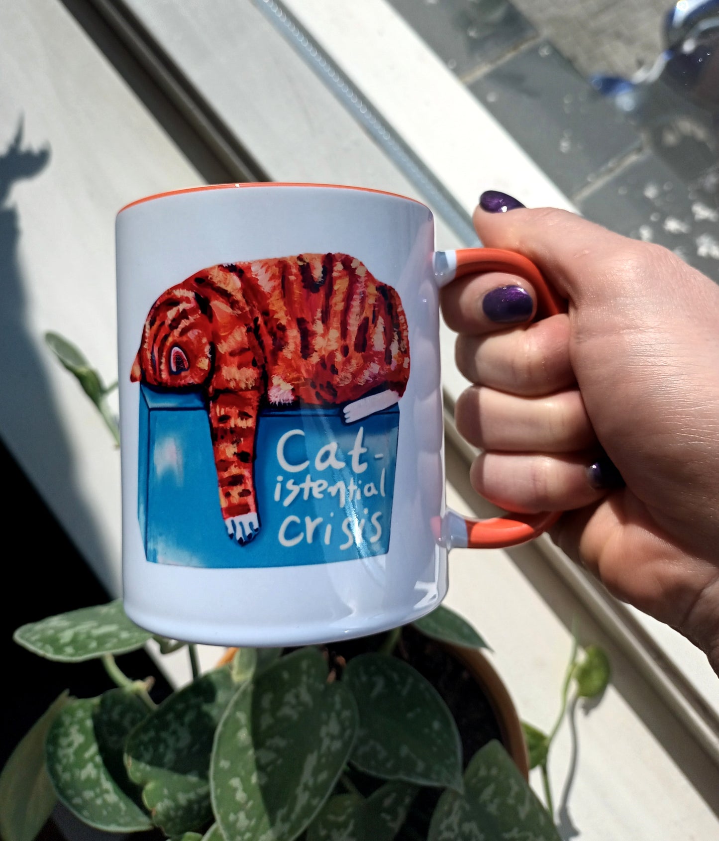 Catistential Crisis" mug featuring an orange cat in deep thought. Handmade ceramic mug with an orange handle and interior. Perfect for cat lovers and coffee enthusiasts. Dishwasher and microwave safe, held by hand.
