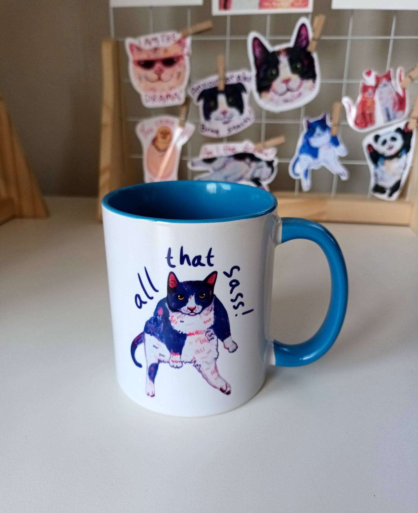 "All That Sass" mug featuring a sassy sitting cat. Handmade ceramic mug with a bold blue handle and interior. Perfect for cat lovers and coffee enthusiasts. Dishwasher and microwave safe.