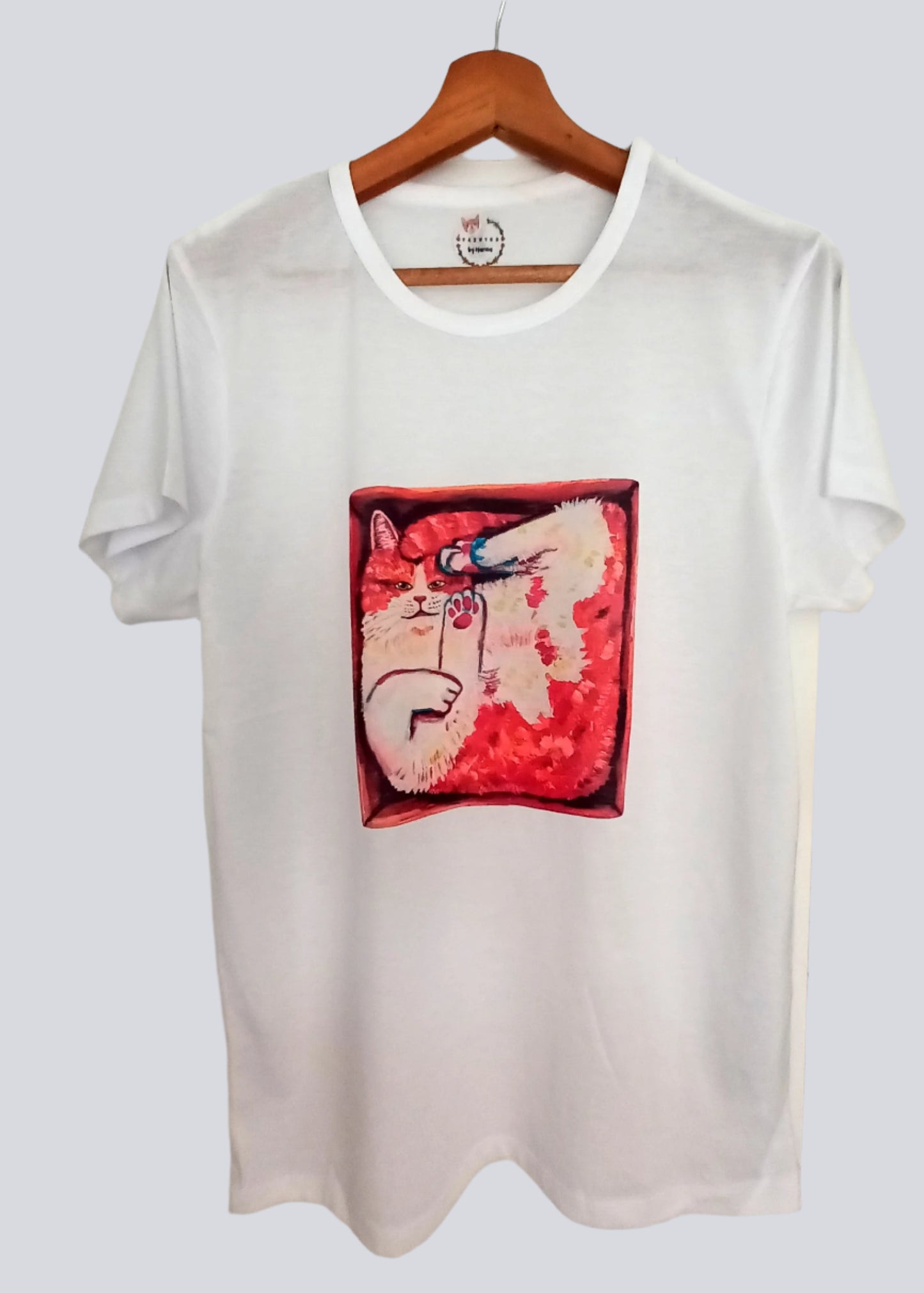 White T-shirt featuring a hand-painted orange cat sitting in a cardboard box – sublimation printed design, t-shirt on a hanger.