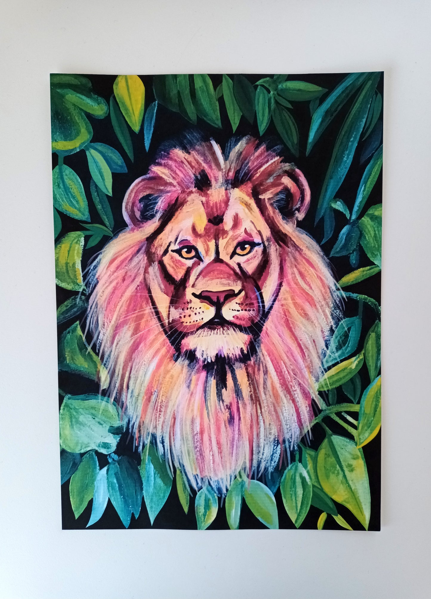 A4 art print of a colourful lion surrounded by green jungle leaves on a table, printed on eco-friendly matte paper.
