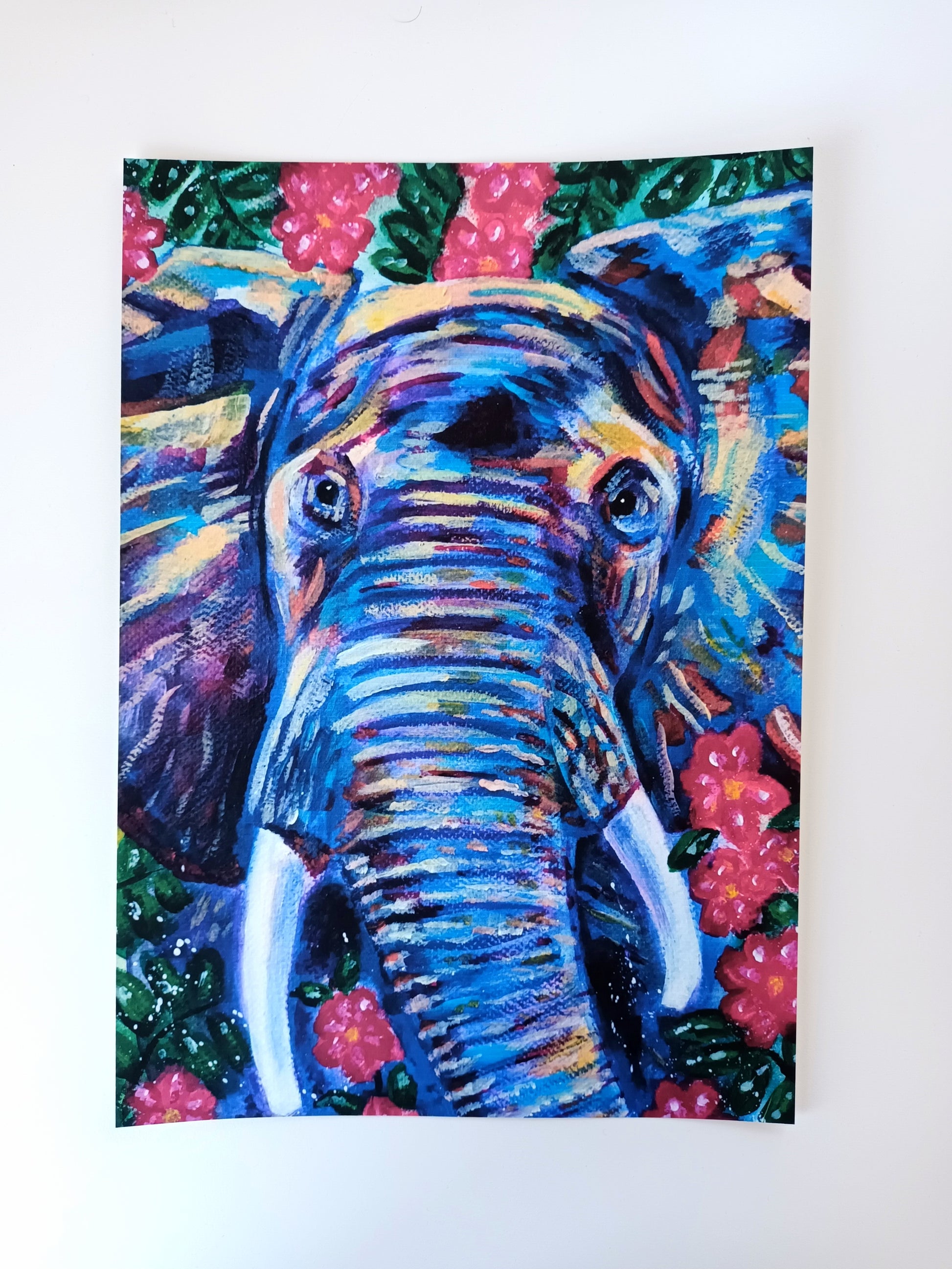 A4 art print of a colourful elephant surrounded by vibrant leaves and flowers on a table, printed on eco-friendly matte paper.