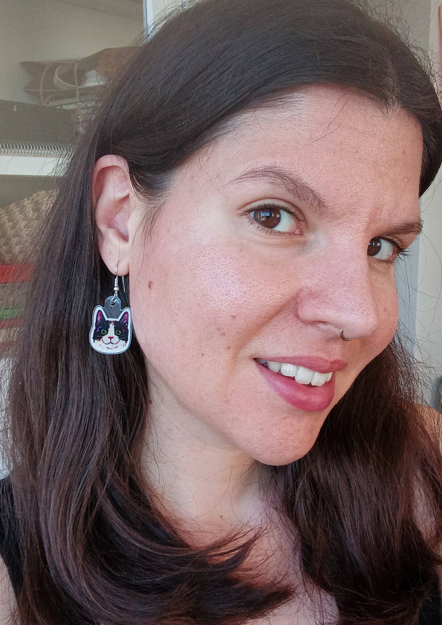 Person wearing handmade earrings with smiling black tuxedo cat faces, stainless steel, approximately 2.5 x 2.5 cm.