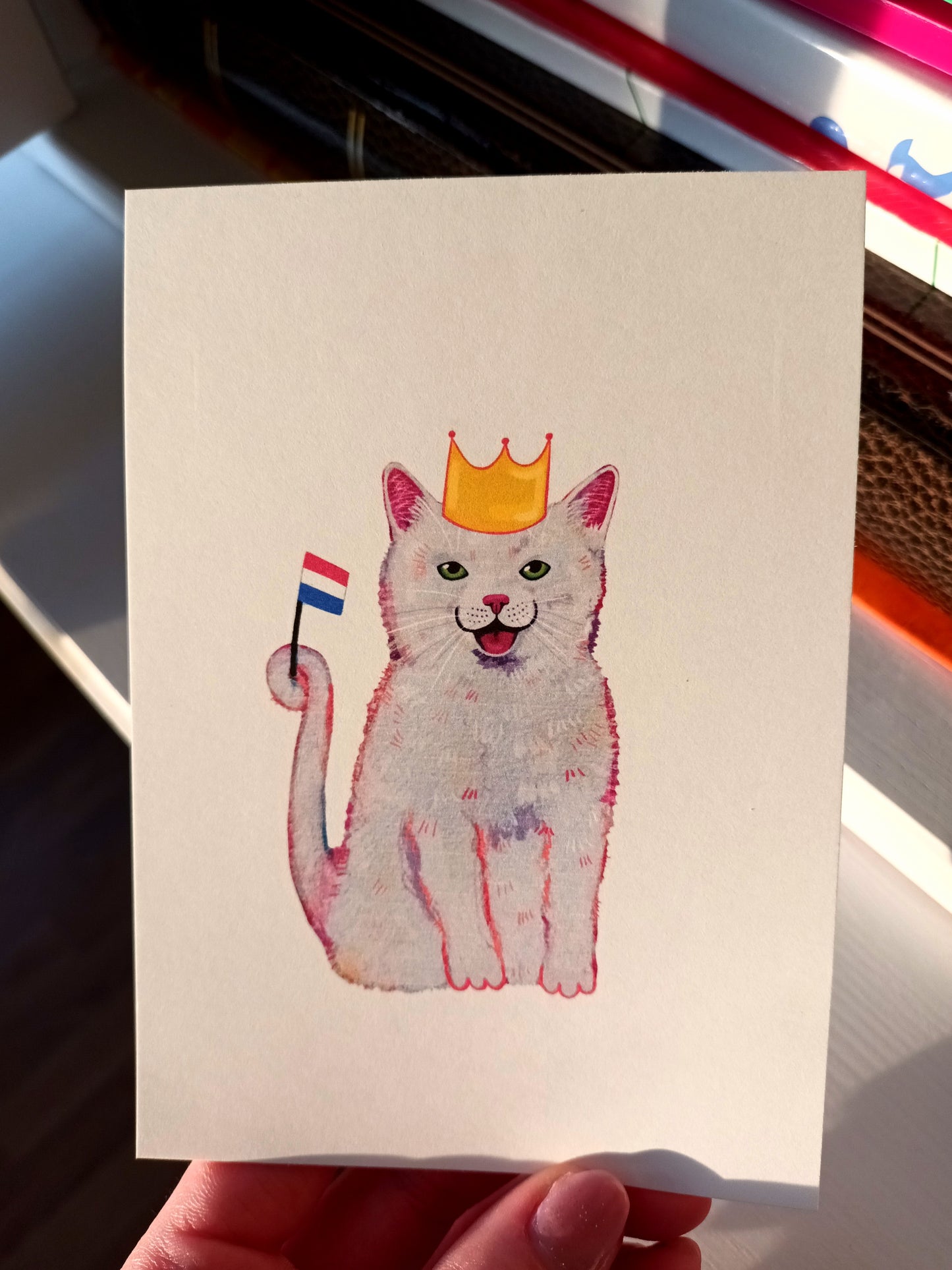 Handmade King’s Day postcard featuring a cute cat wearing a golden crown, printed on eco-friendly paper, perfect for celebrating Koningsdag, held by hand.