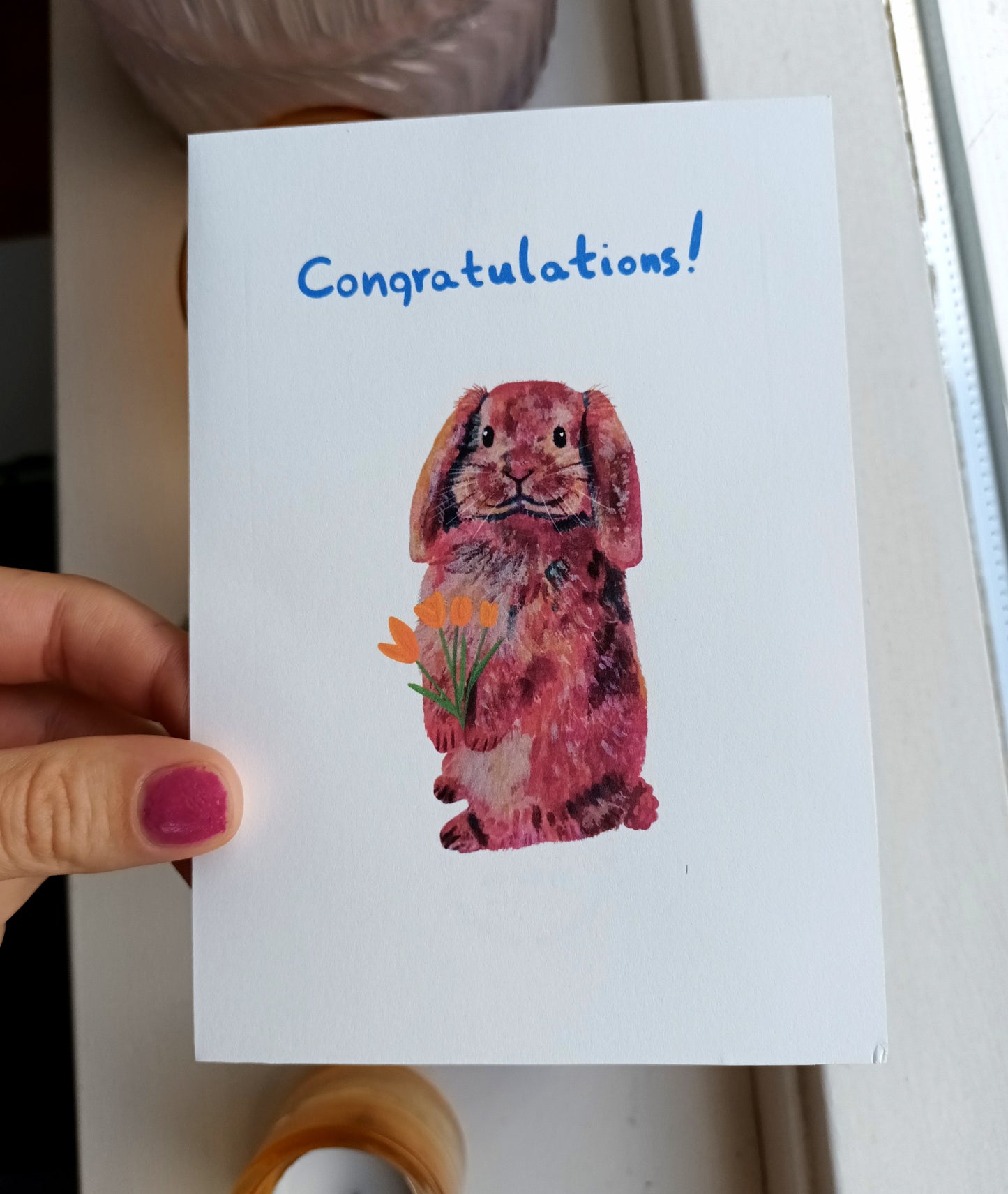 Card with a rabbit illustration and 'Congratulations!' text held by a hand.