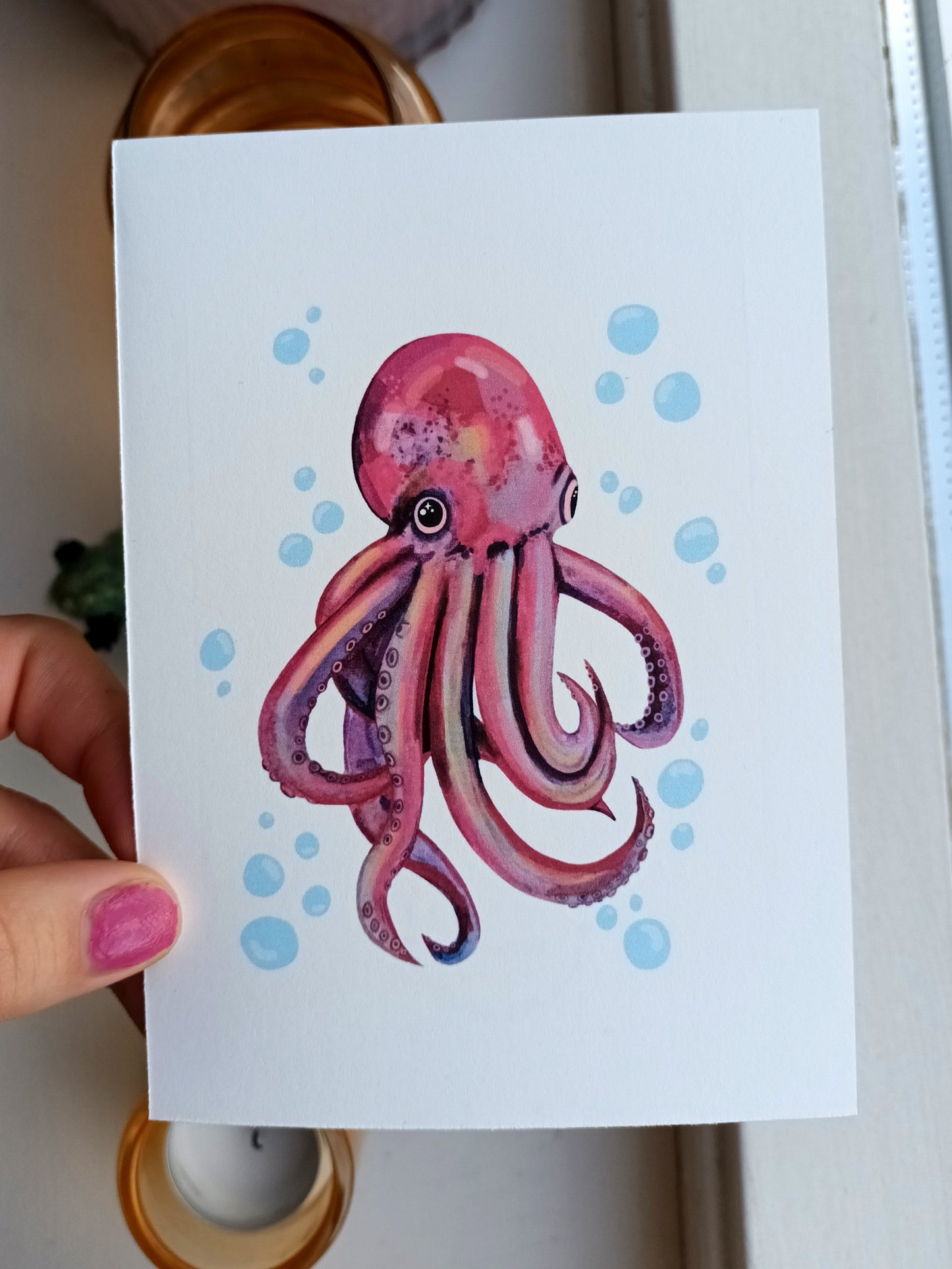 Card with a pink octopus illustration held by a hand.