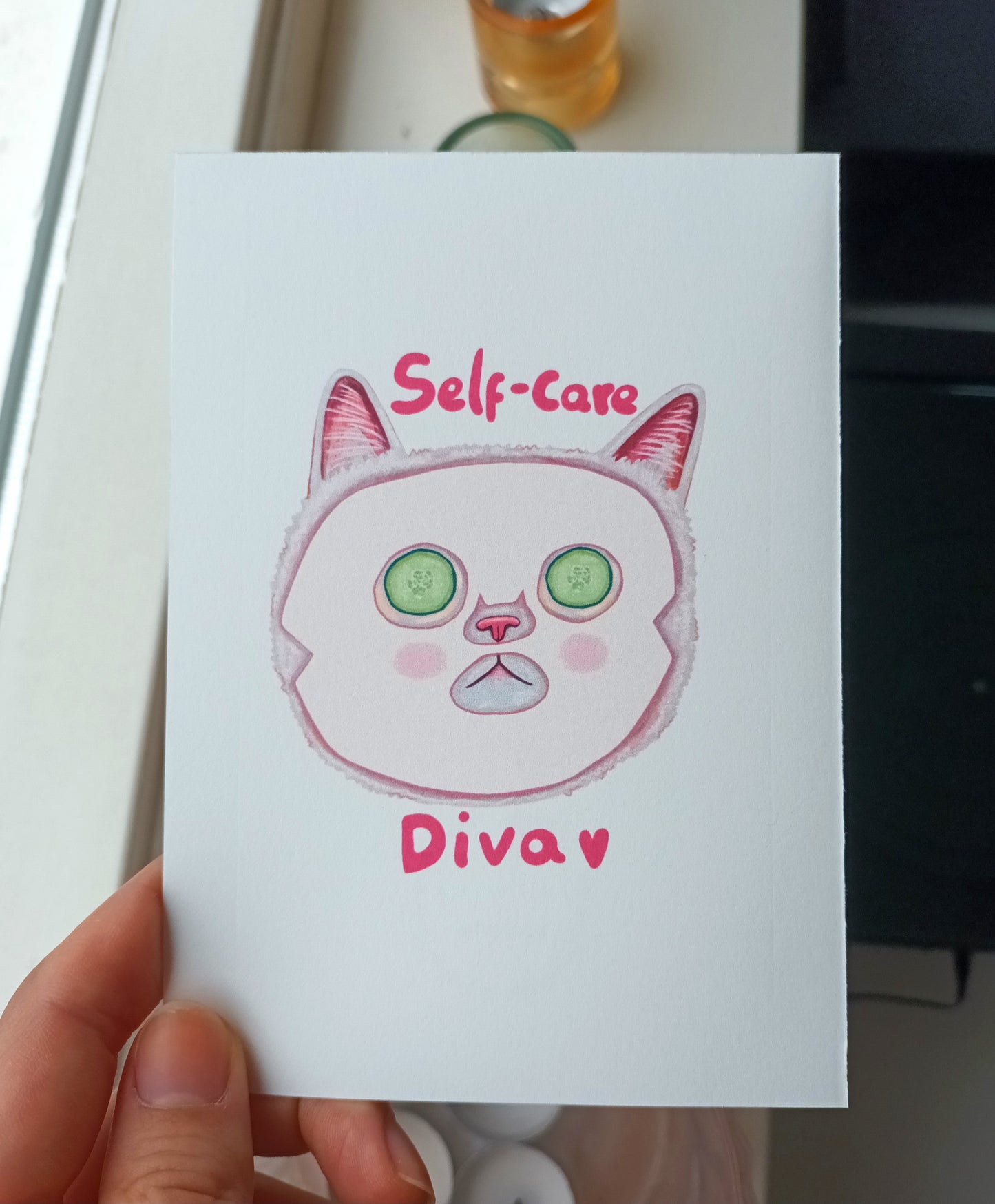 Card with a cat illustration and 'Self-care Diva' text held by a hand.