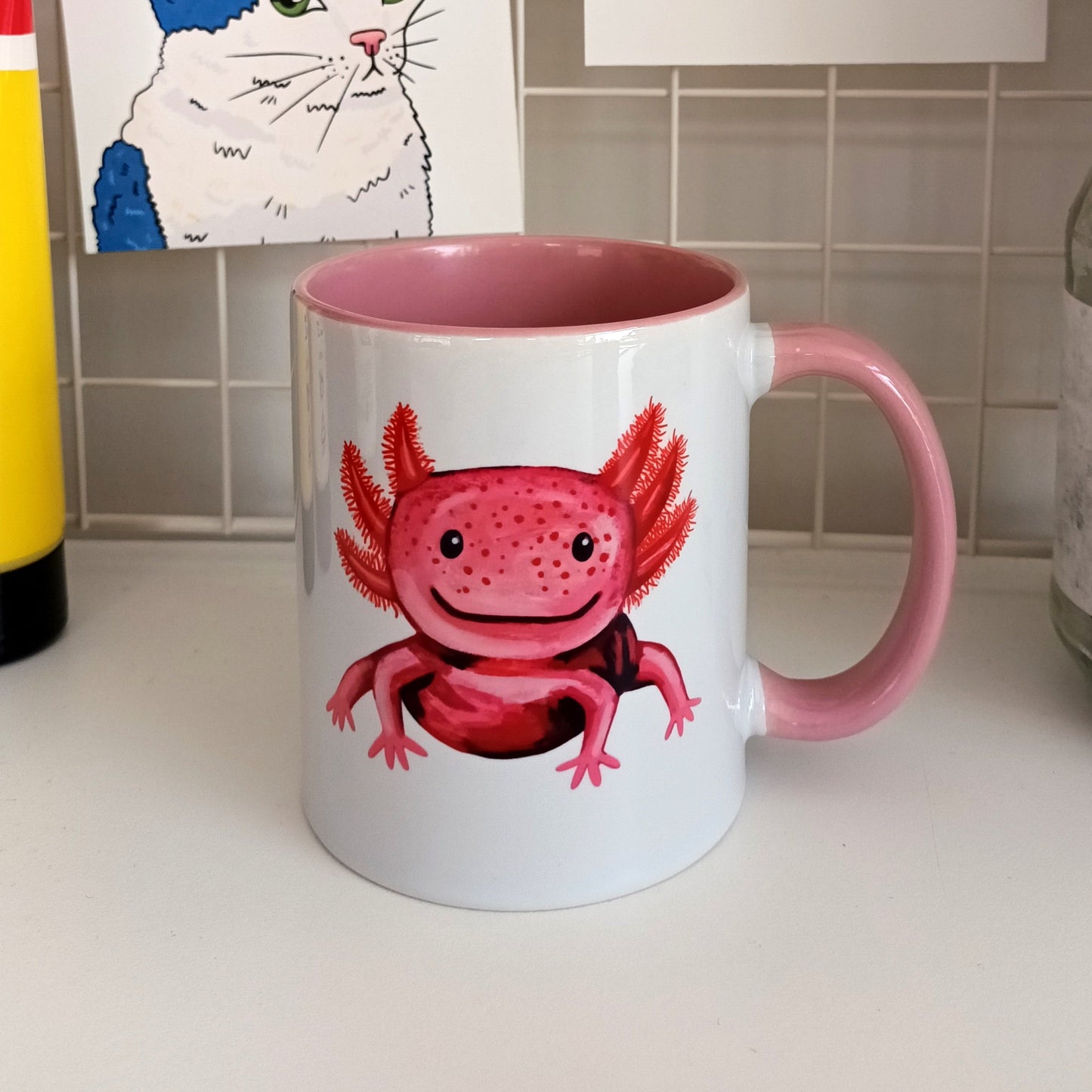 Handmade ceramic mug with a cute pink axolotl illustration, pink handle and interior.