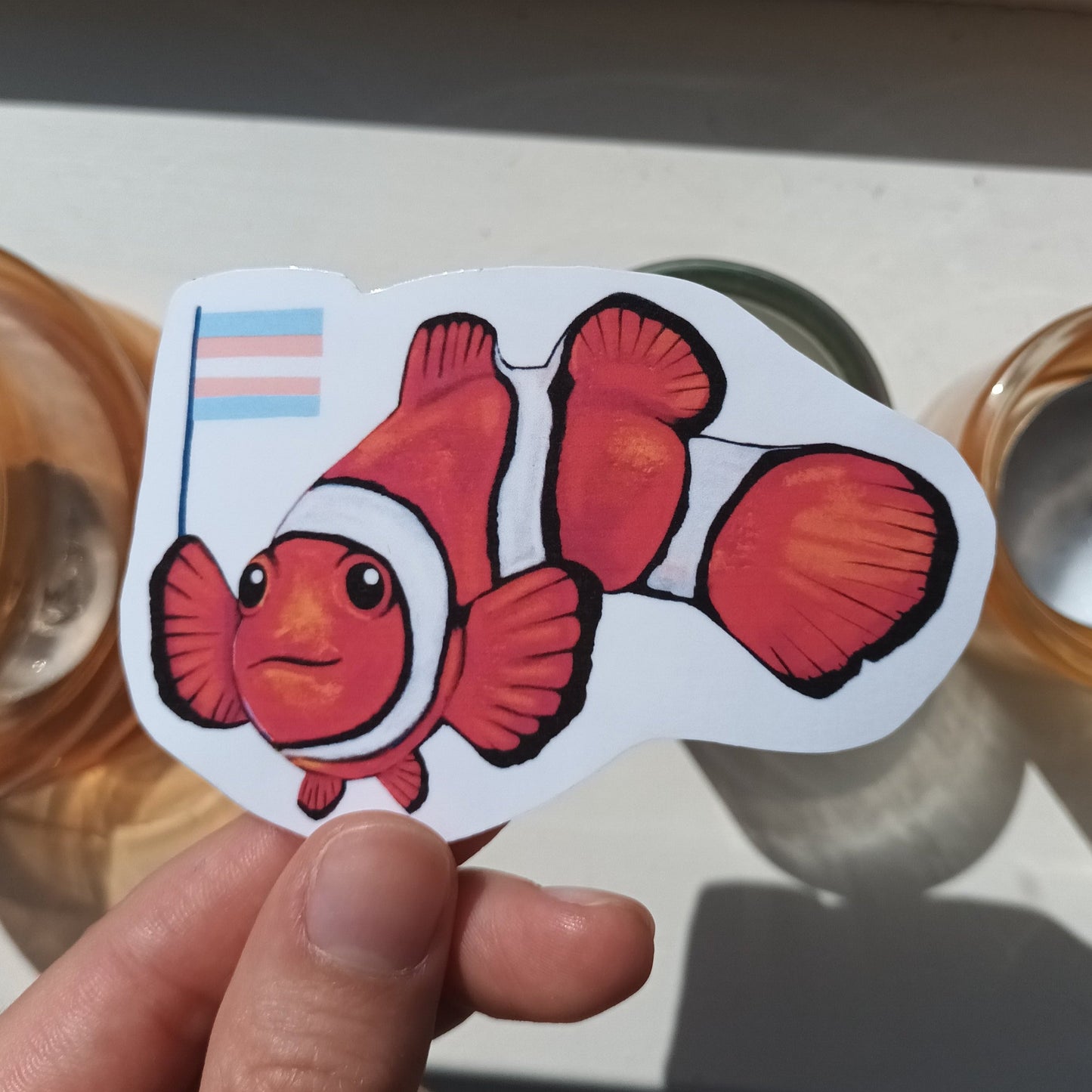 Clownfish holding trans flag sticker – handmade LGBTQ+ pride vinyl sticker.