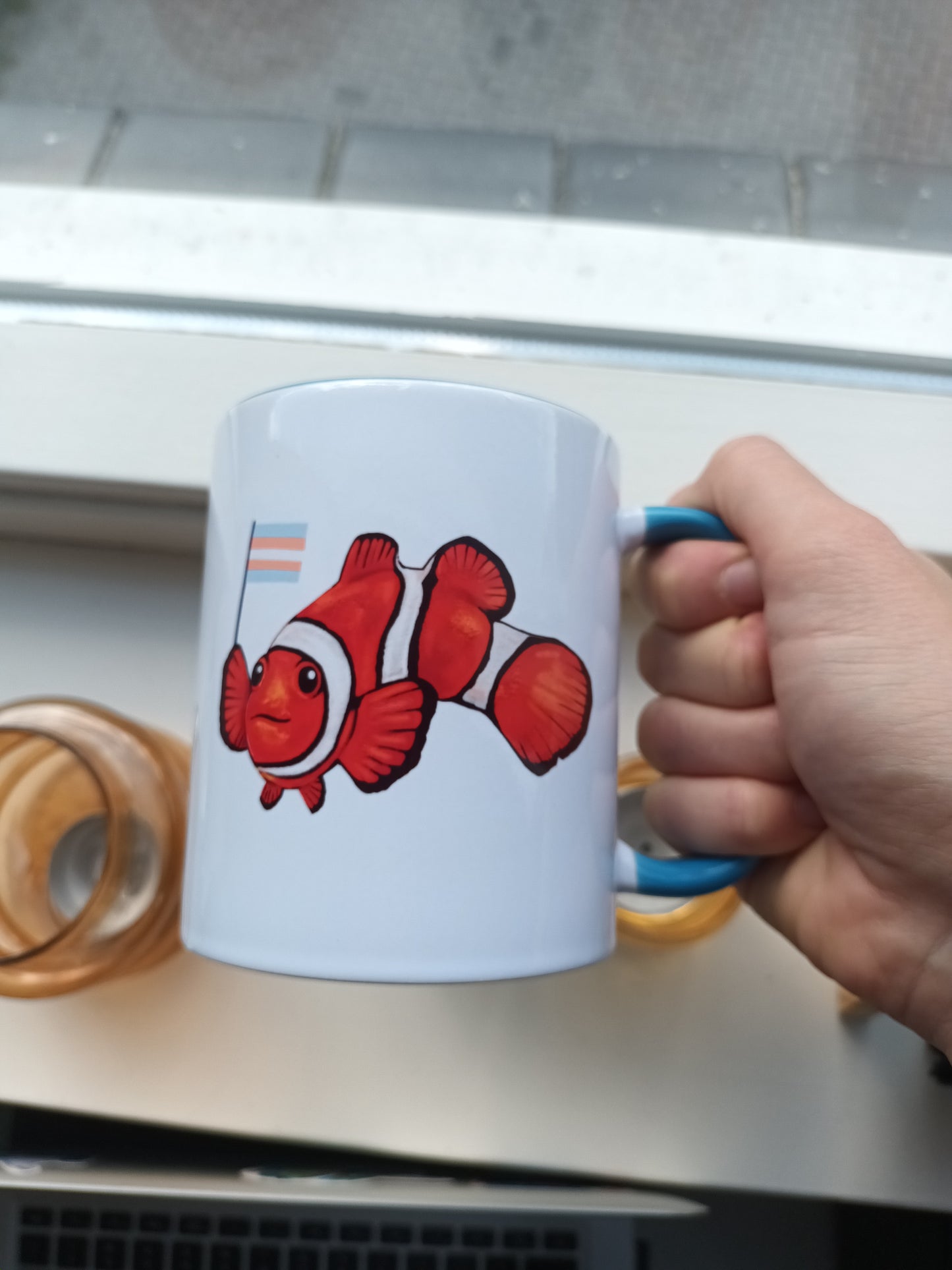 Hand holding a white mug with a clown fish design against a neutral background
