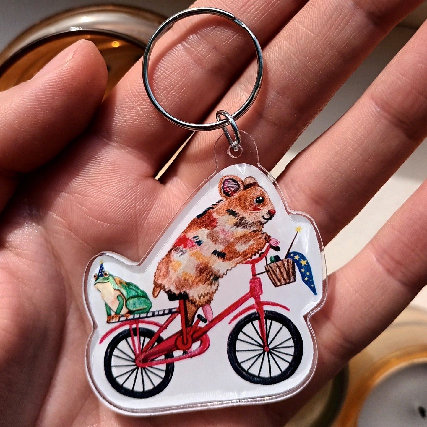 Keychain with a hamster riding a bicycle design held in a hand.