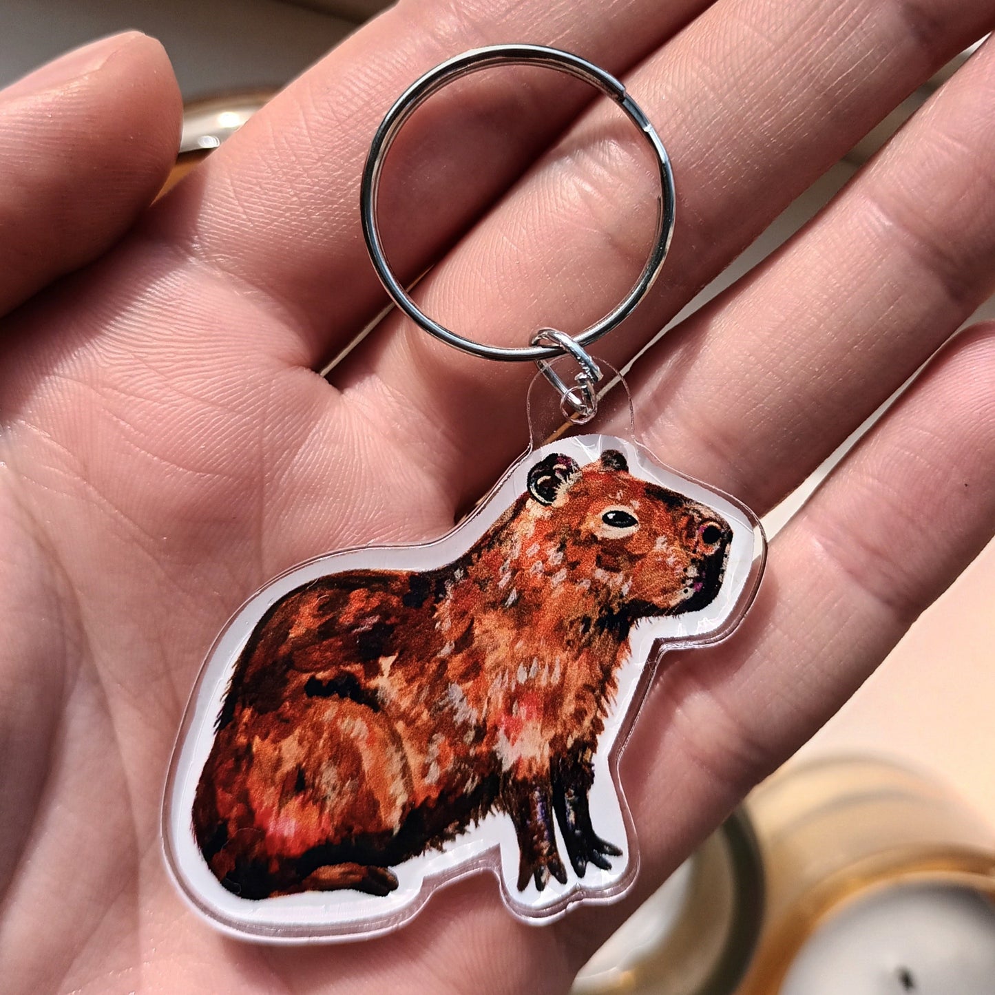 Hand holding a keychain with a capybara design.