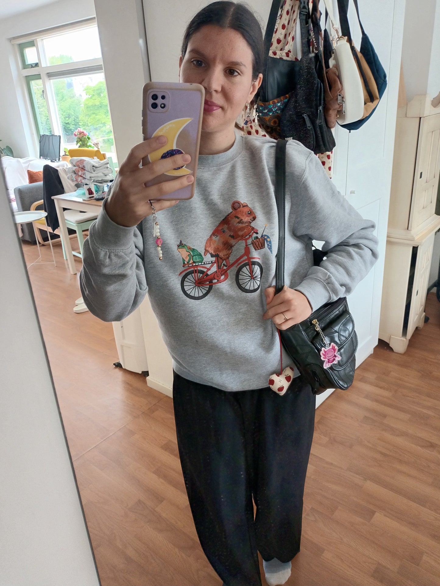 Person wearing light grey eco-friendly sweater with cute hamster cycling and frog familiar design, made from organic cotton and recycled polyester.