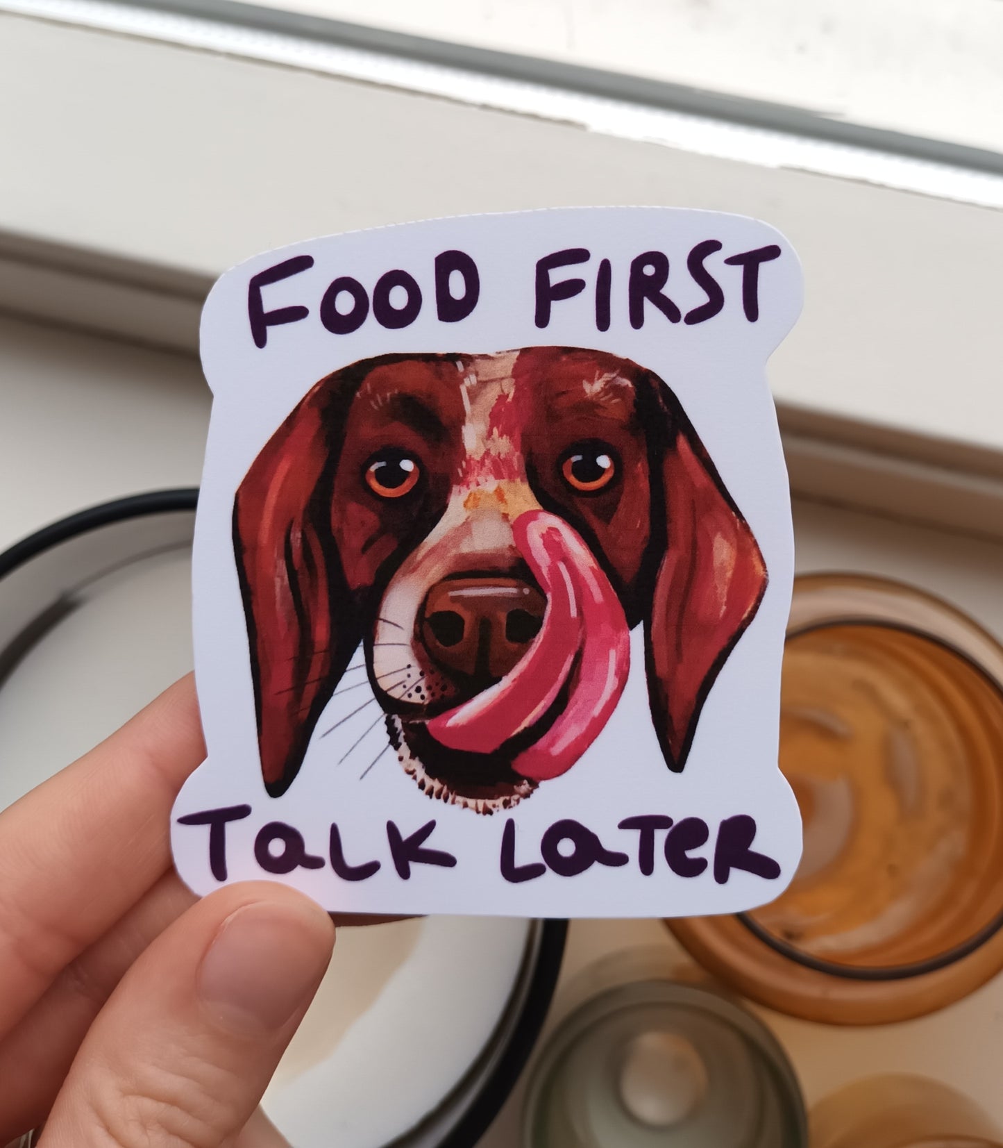 Dog Licking His Snout sticker with “Food First, Talk Later” text, original illustration by the artist, 7 x 7.87 cm