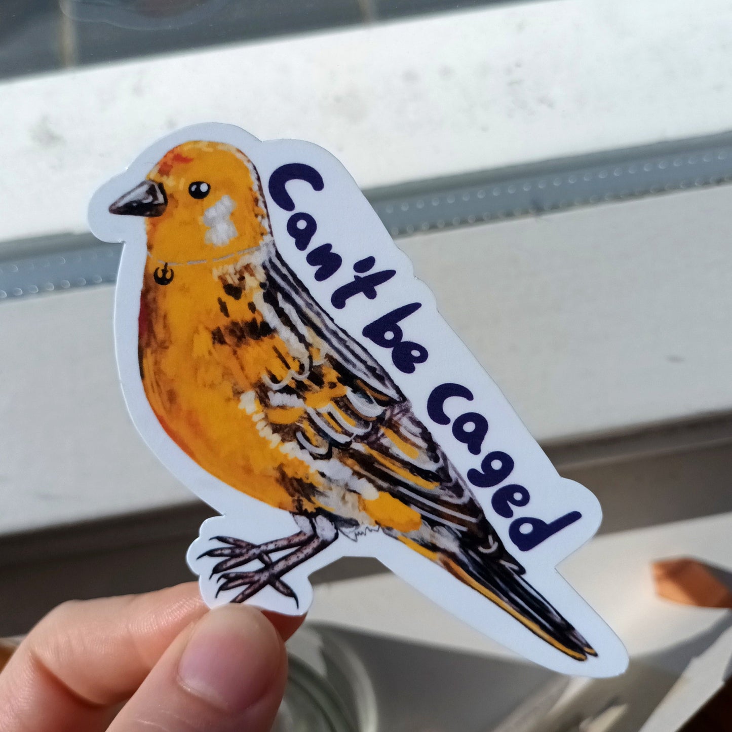 Sticker of a bird with 'Can't be caged' text held by a hand.