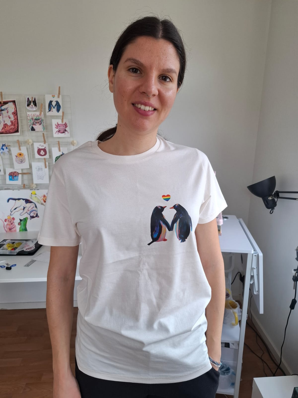 Person wearing a white t-shirt with penguins and rainbow heart design