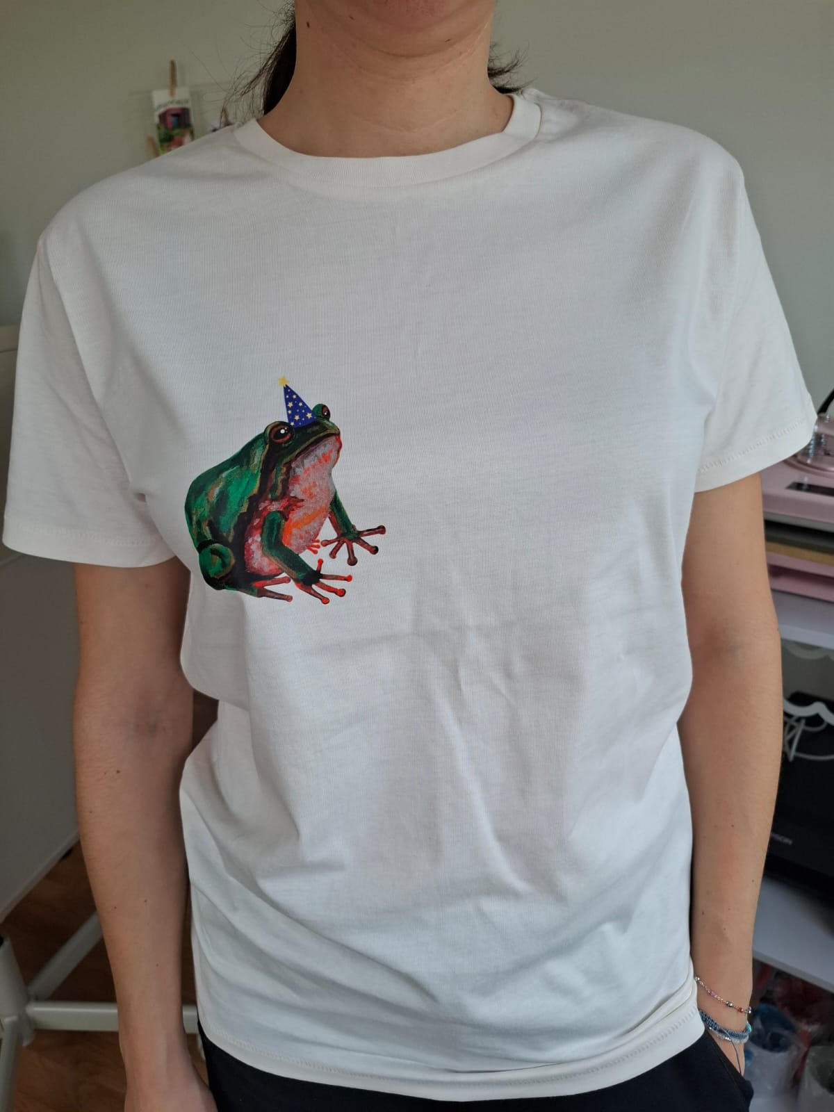 Person wearing a white t-shirt with a colorful frog graphic on a plain background