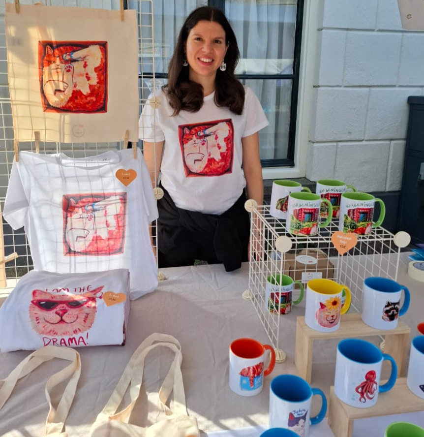 Handmade market stall at Wageningen Saturday Market with colourful animal-themed art, mugs, and gifts by a local artist.