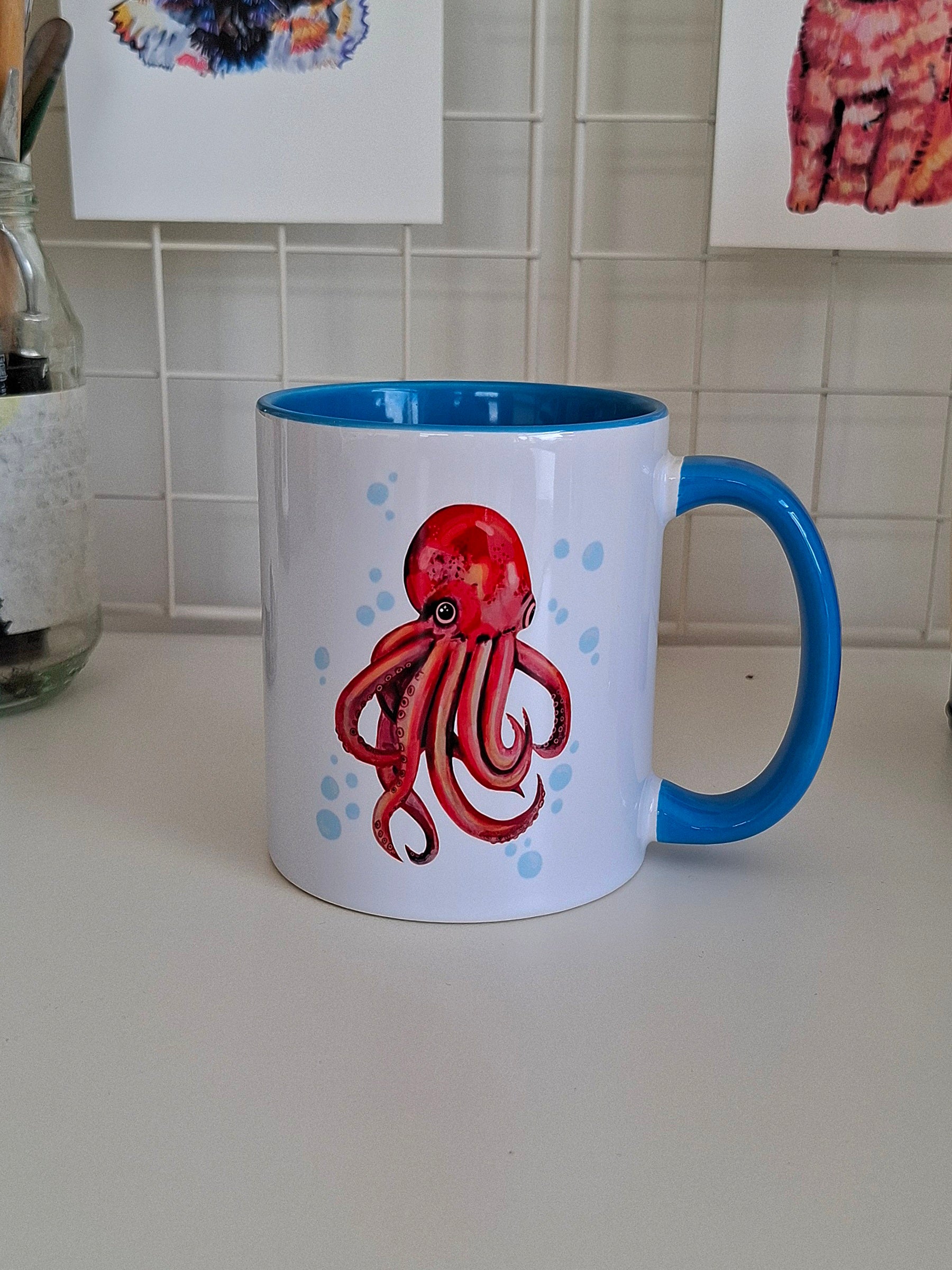 Colourful octopus design printed on a white ceramic mug with blue handle and interior, handmade by the artist