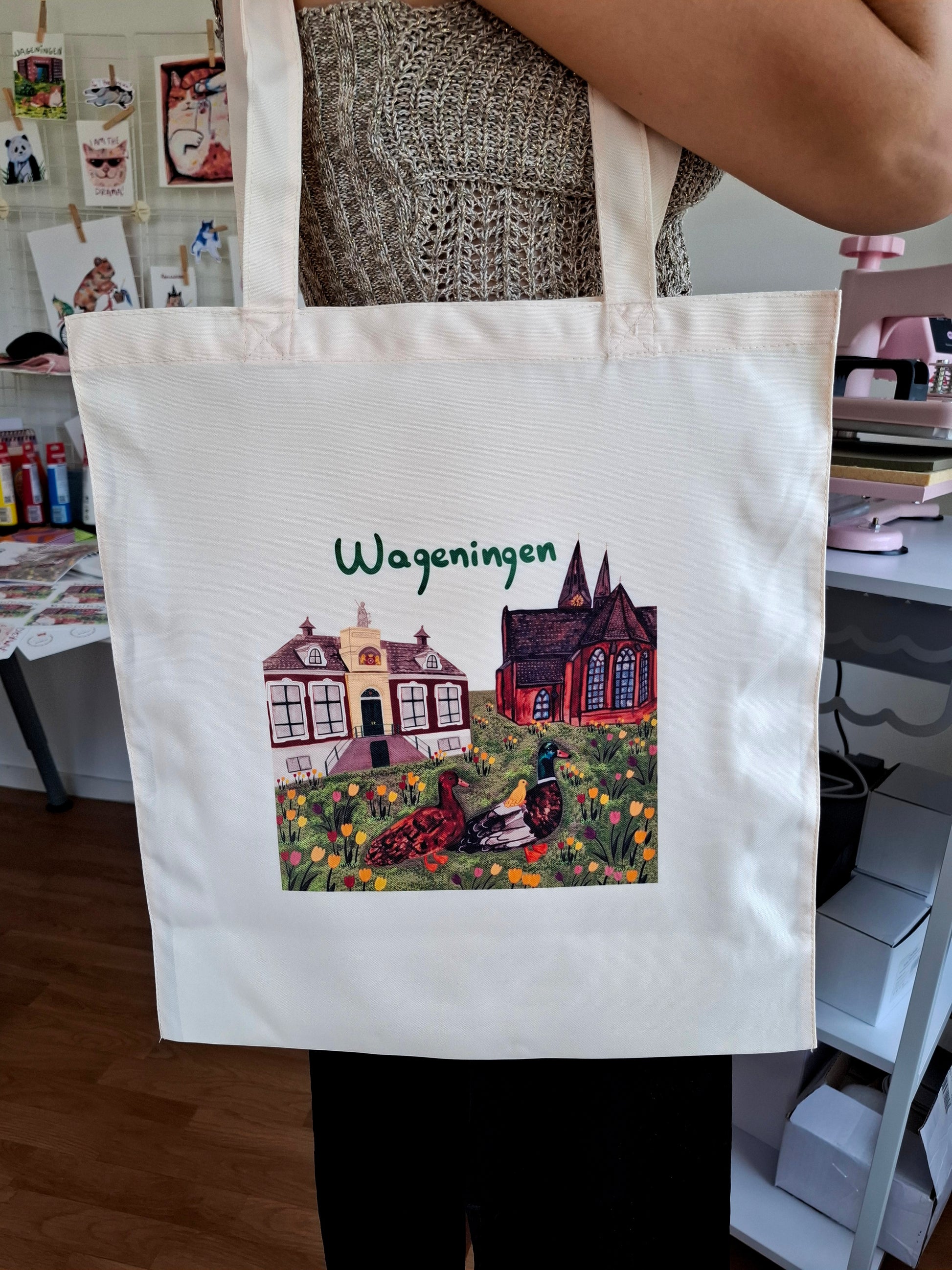 Tote bag with a printed design and 'Wageningen' text held by a person in an indoor setting.