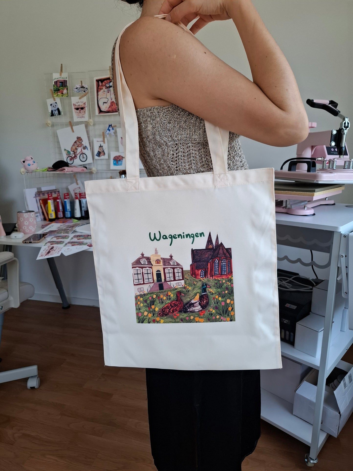 Person holding a tote bag with a printed Wageningen design and text, sitting in a casual setting.