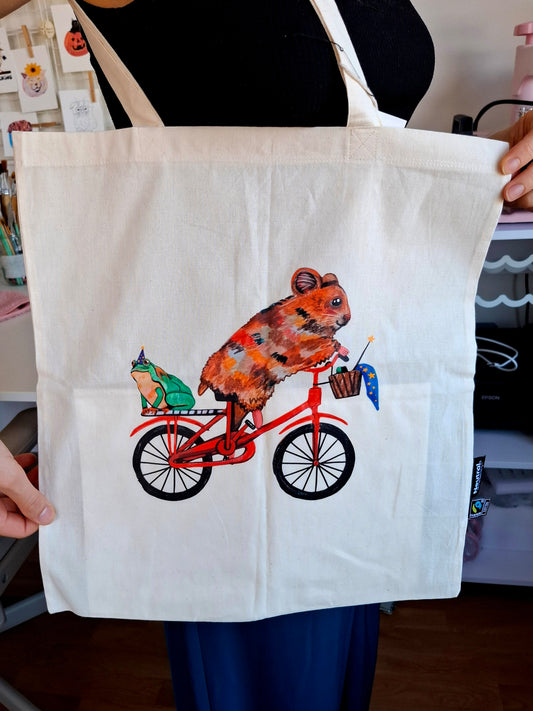 Organic cotton tote bag with cute hamster on a bike and frog design, eco-friendly.