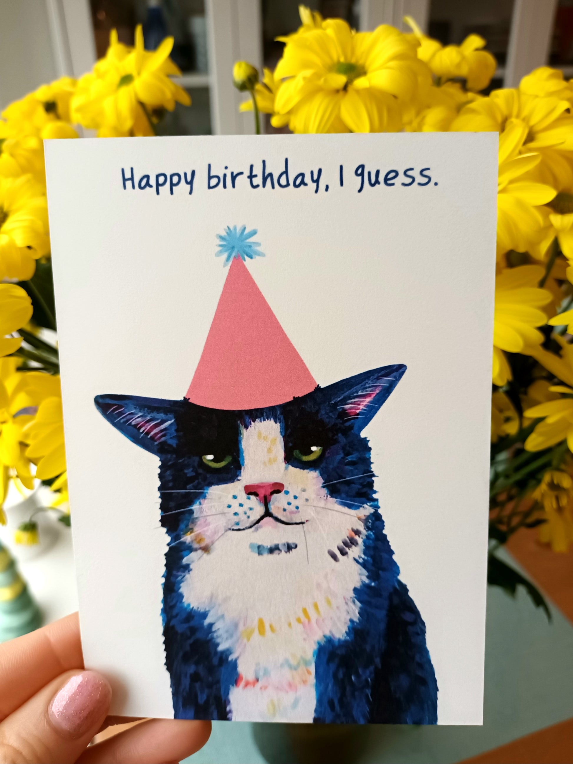 Funny Happy Birthday greeting card featuring a sassy tuxedo cat with ‘Happy Birthday, I Guess’ text, printed on eco-friendly paper held in hand