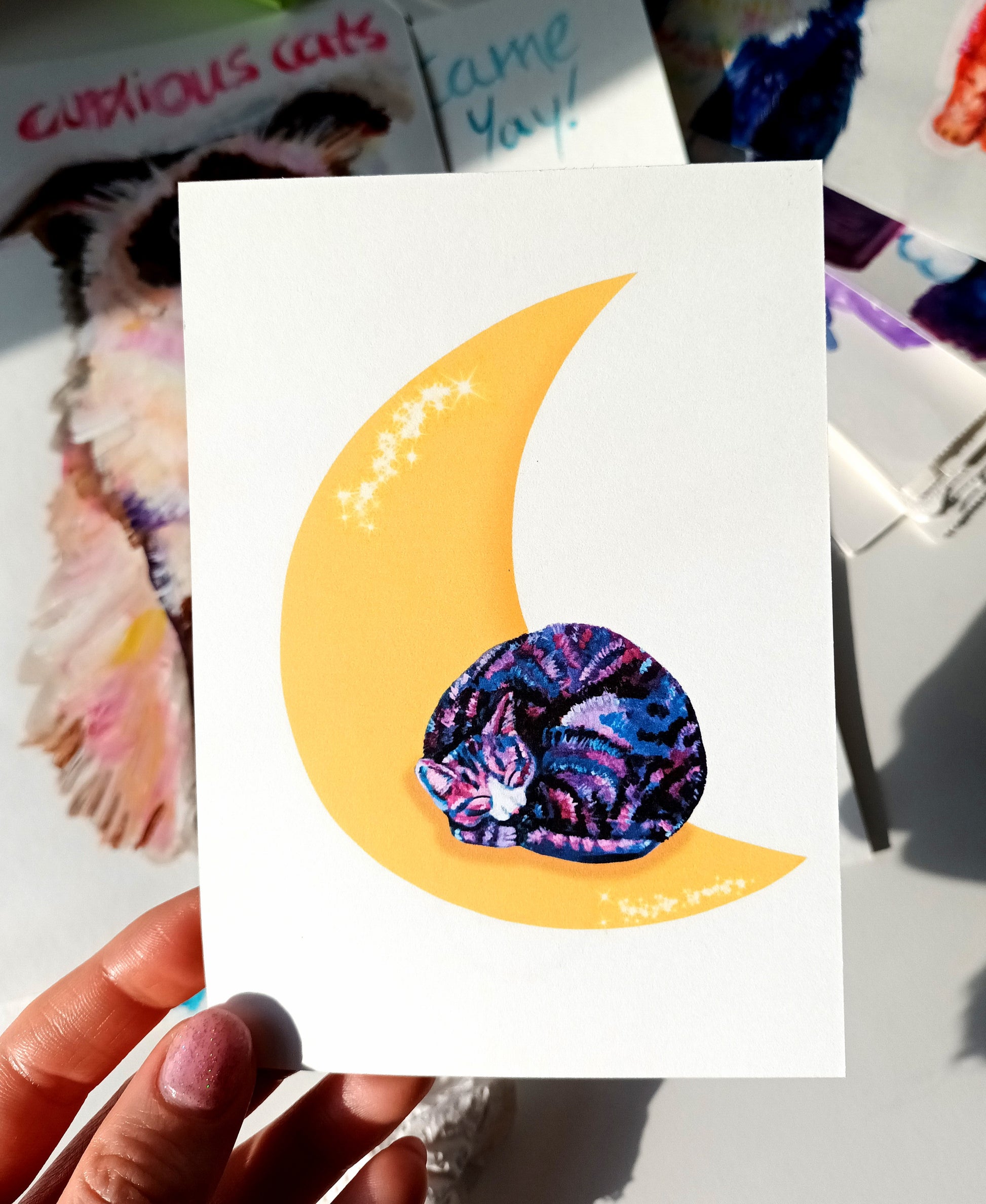 Handmade celestial postcard featuring a dreamy purple cat sleeping on a crescent moon, high-quality illustration art card held by hand