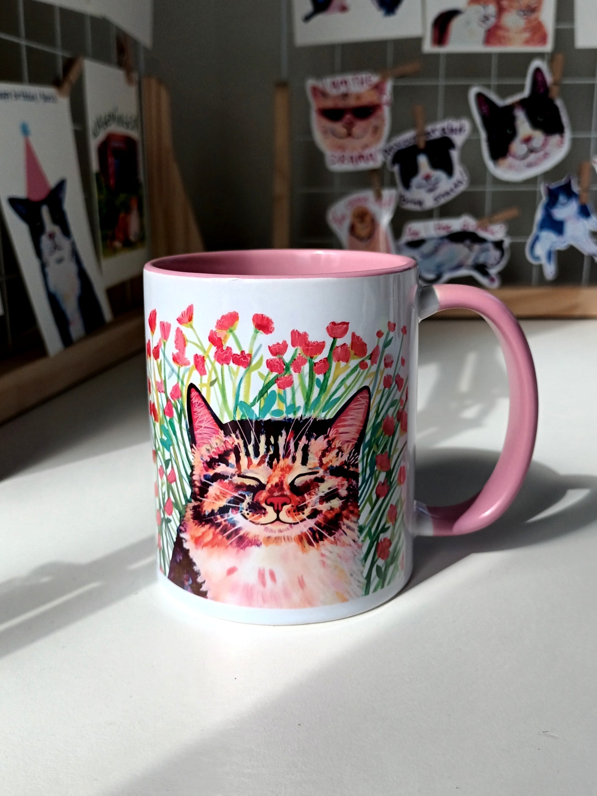 Handmade mug with a cute cat sitting in a meadow of pink flowers, pink handle and inside.