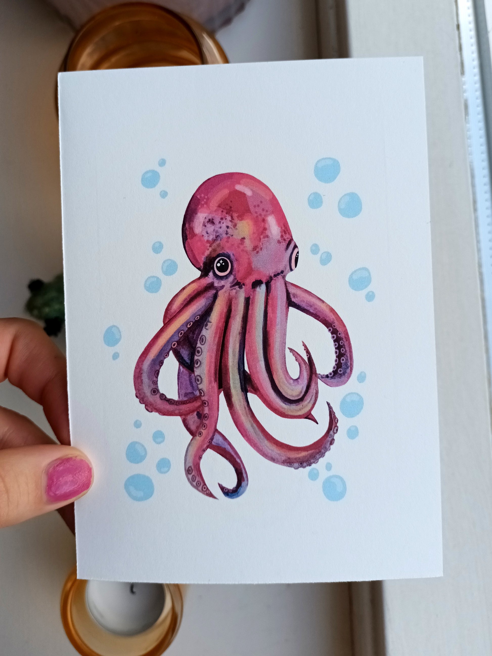 Card with a pink octopus illustration held by a hand.