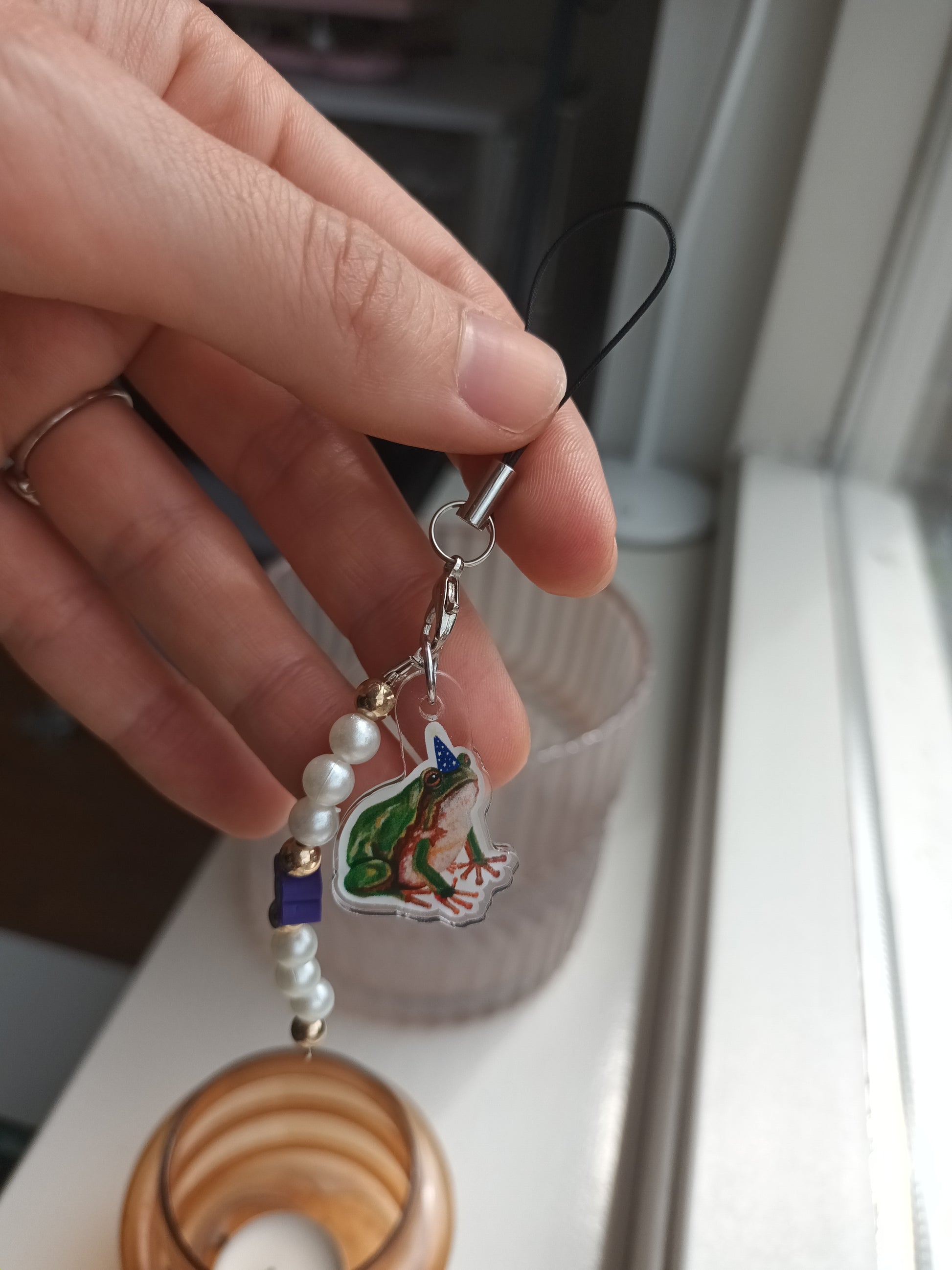 Hand holding a keychain with a colourful frog charm and beads against a blurred background