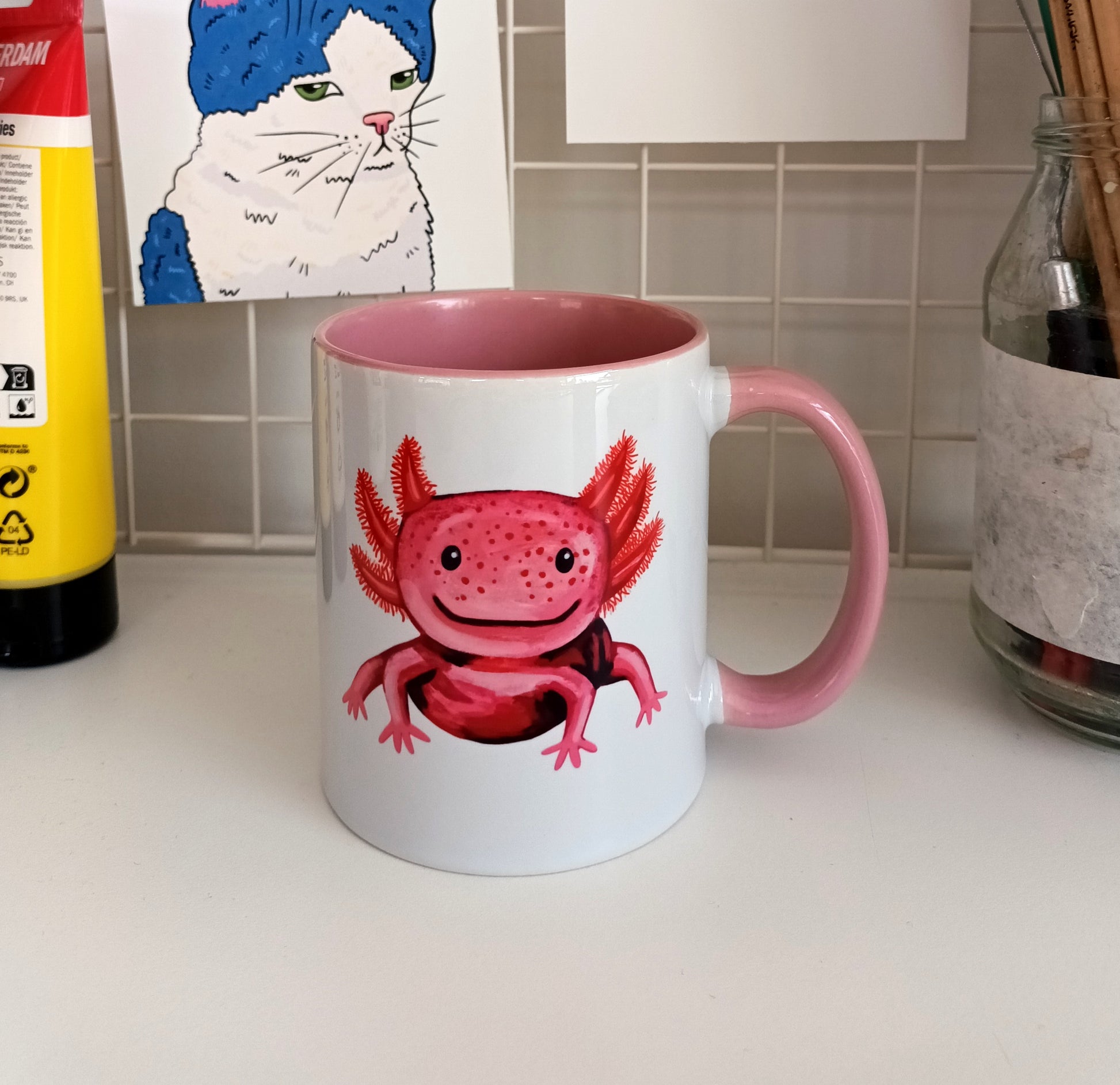 Handmade ceramic mug with a cute pink axolotl illustration, pink handle and interior.