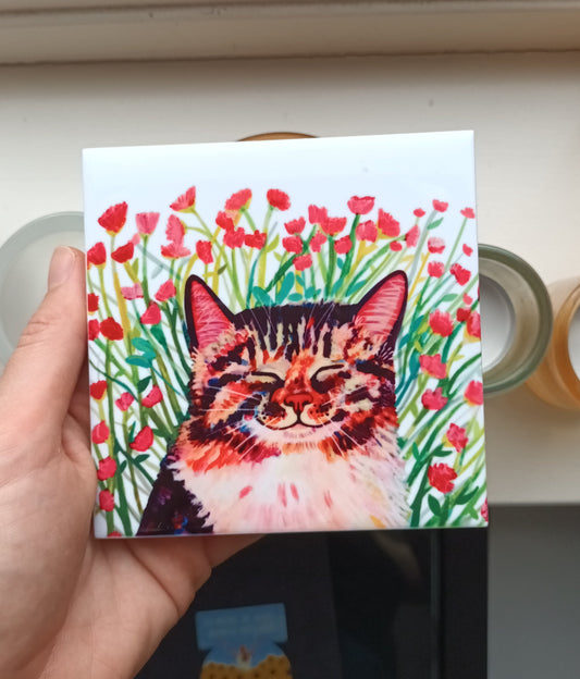 Hand holding a tile with a colourful cat illustration on a blurred background