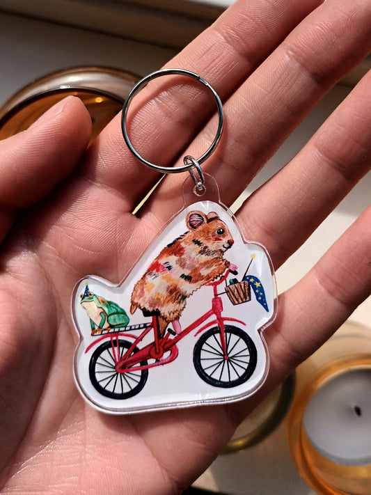 Keychain with a hamster riding a bicycle design held in a hand.