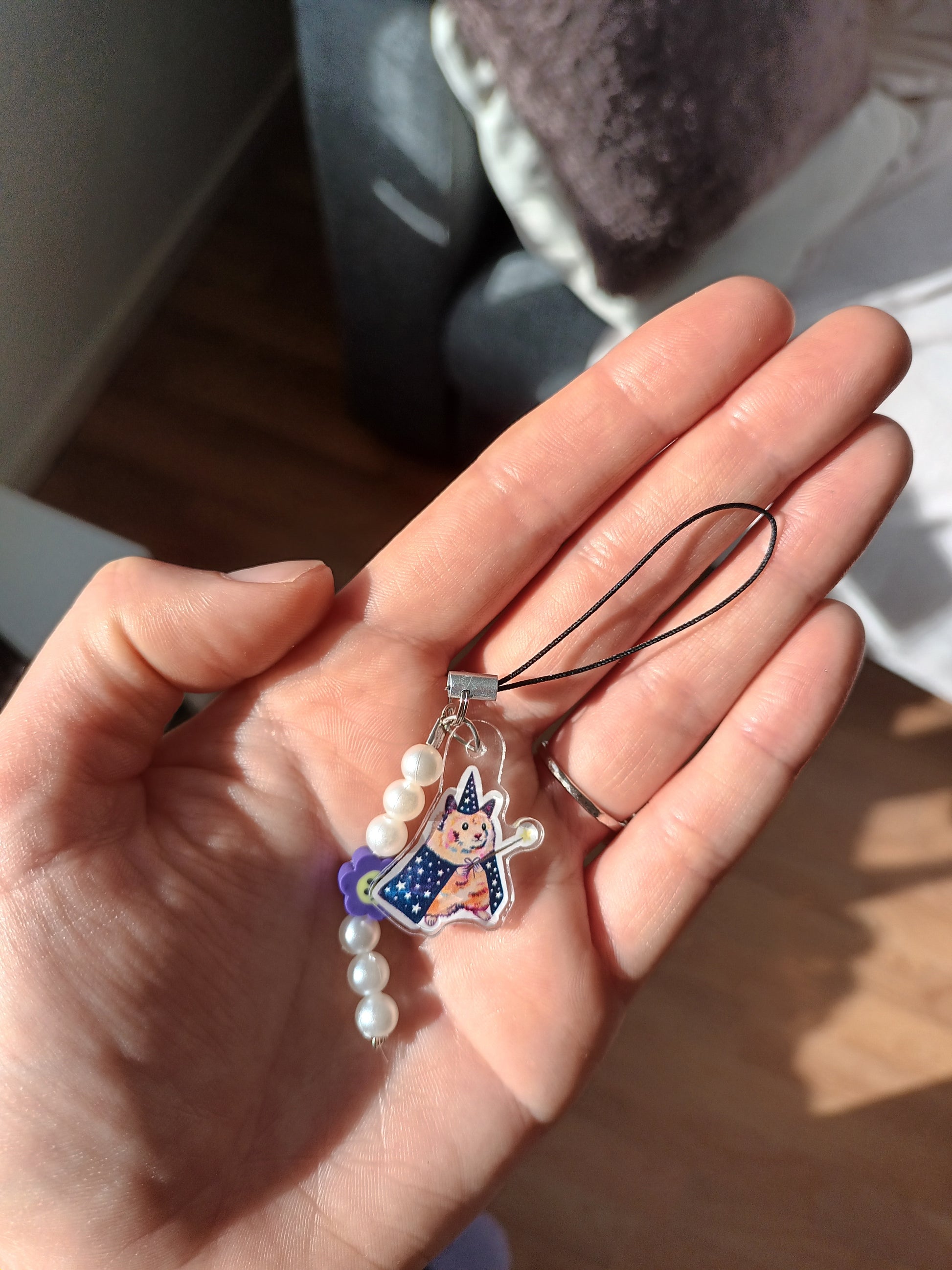 Hand holding a decorative phone charm with a character design and pearls.