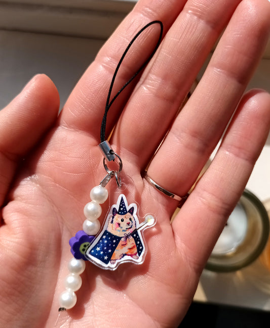 Hand holding a small phone charm charm with a hamster wizard, and pearls.