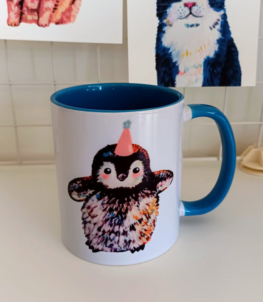 Mug with a penguin design wearing a party hat on a kitchen counter.