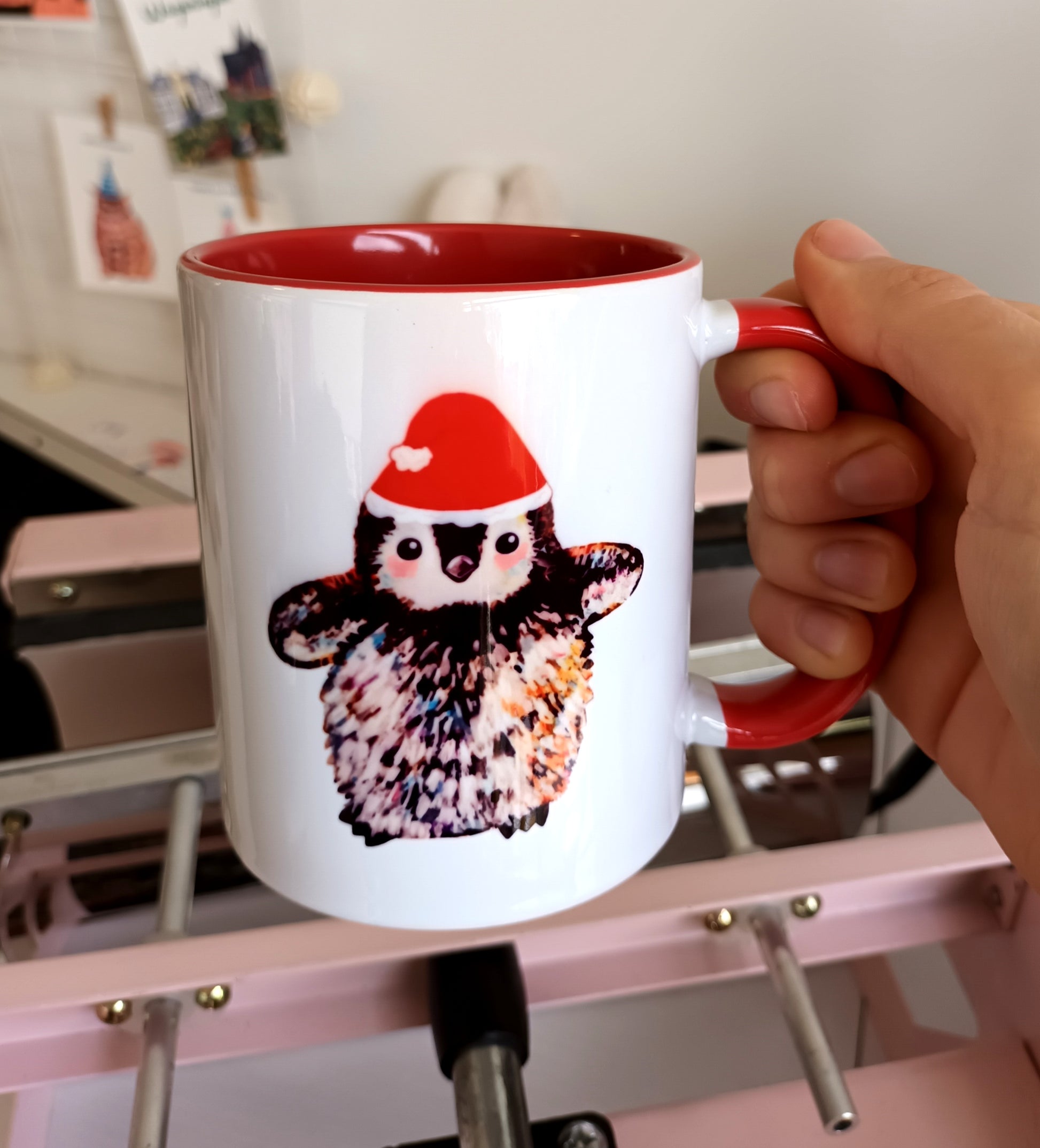 Handmade ceramic mug with small penguin wearing Santa hat, red handle and red interior, Christmas-themed mug.