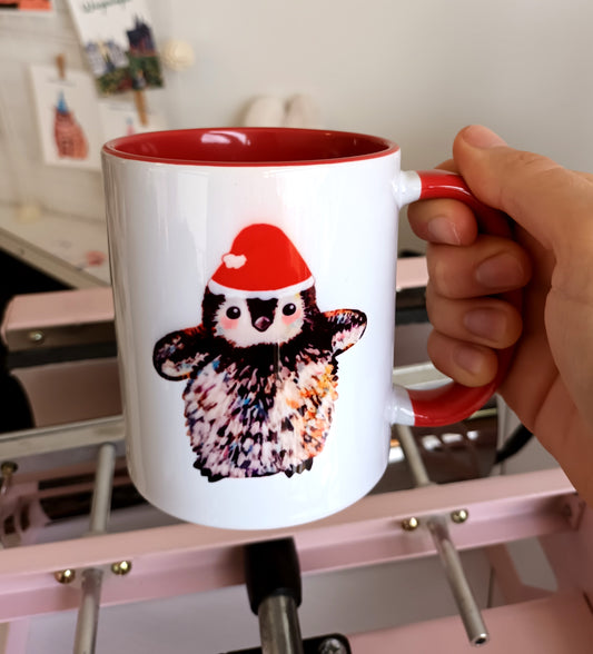 Handmade ceramic mug with small penguin wearing Santa hat, red handle and red interior, Christmas-themed mug.
