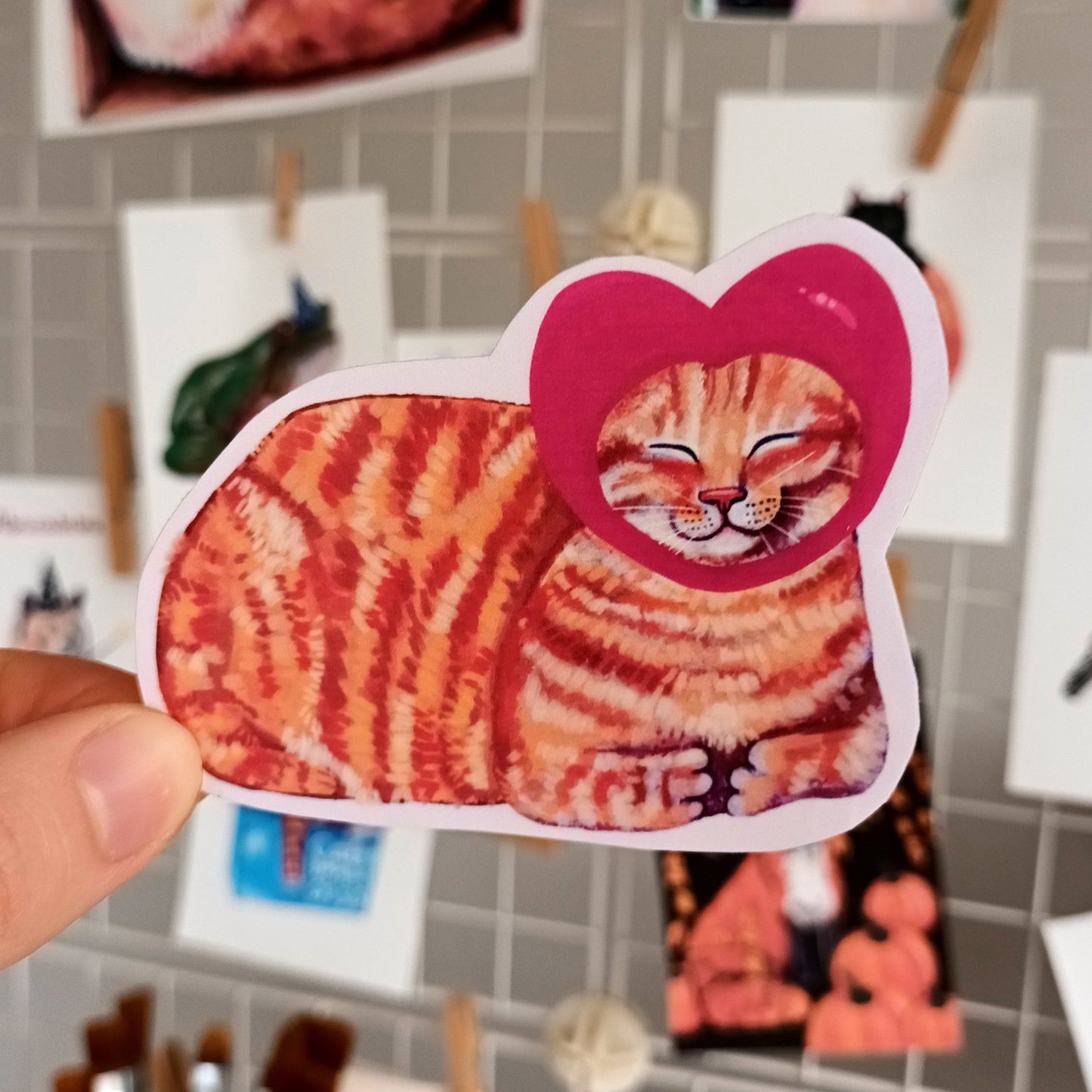 Hand holding a cat-shaped sticker with a heart hat. Cute Valentine's sticker.