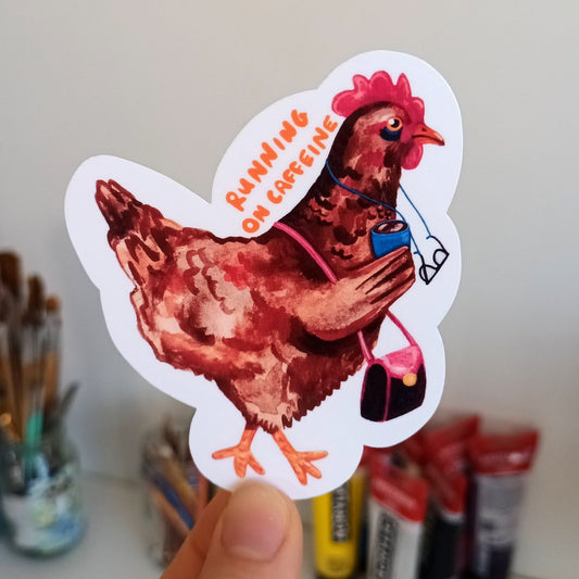 Hand holding a sticker of a chicken drinking coffee.