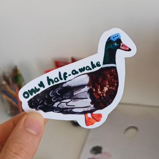 Hand holding a sticker of a duck with 'only half awake' text .
